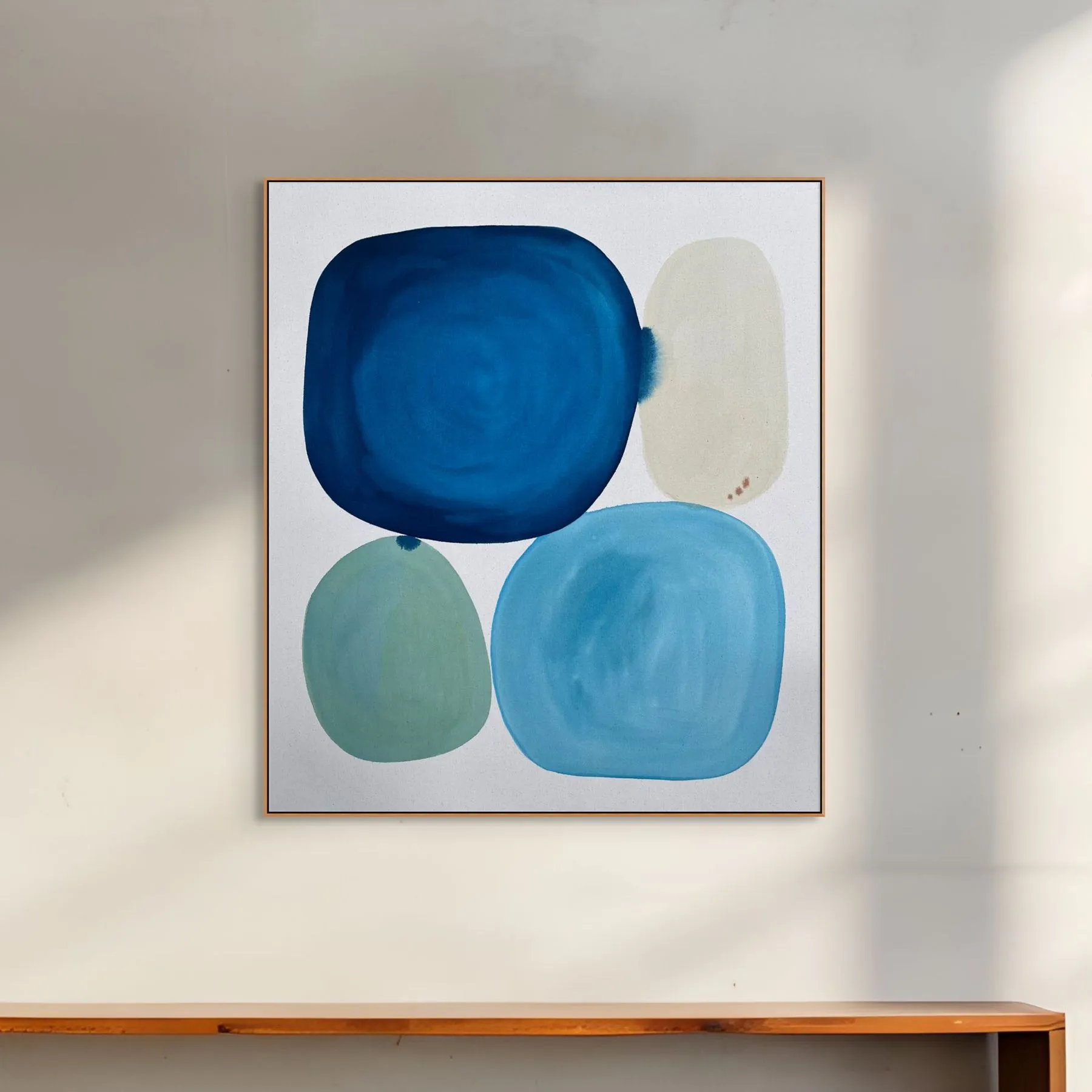 Abstract artwork featuring blue and teal shapes on a white background, displayed in a light-colored frame.