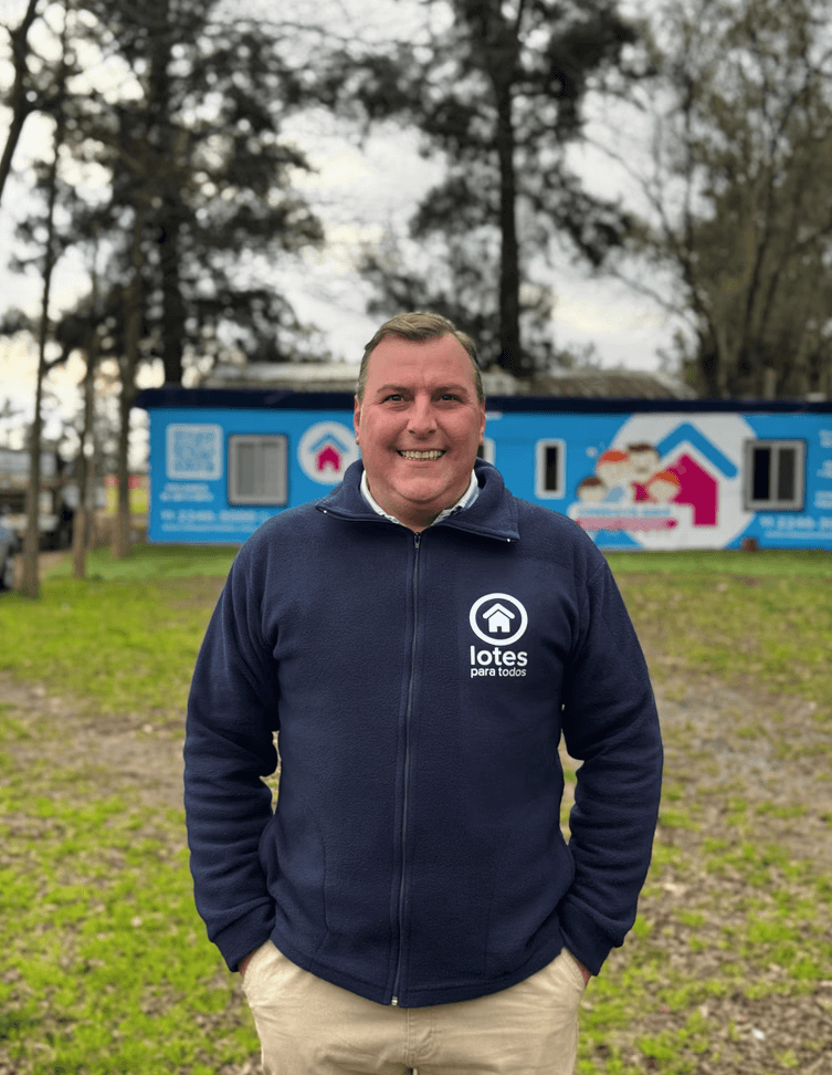 A smiling young man with crossed arms, wearing a plaid shirt and white t-shirt, poses against a dark background.