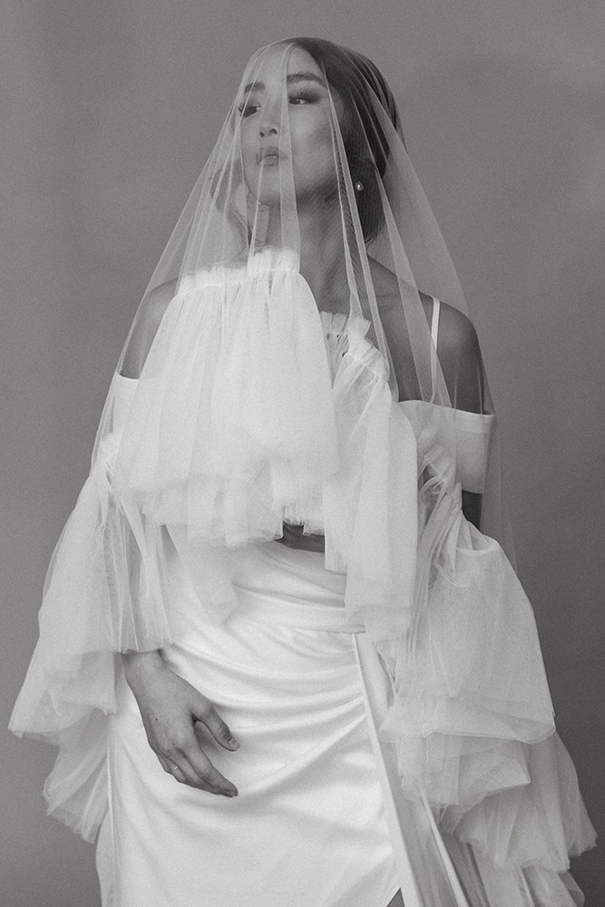 Full-length portrait of a bride beneath a long sheer veil in a flowing white gown, soft light, fine art bridal editorial by Eva Sitko