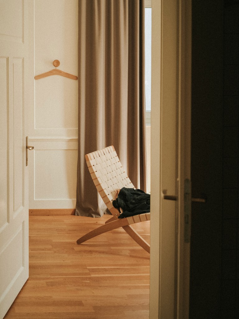 Minimalist beige room with a rounded chair, side table, and potted plant