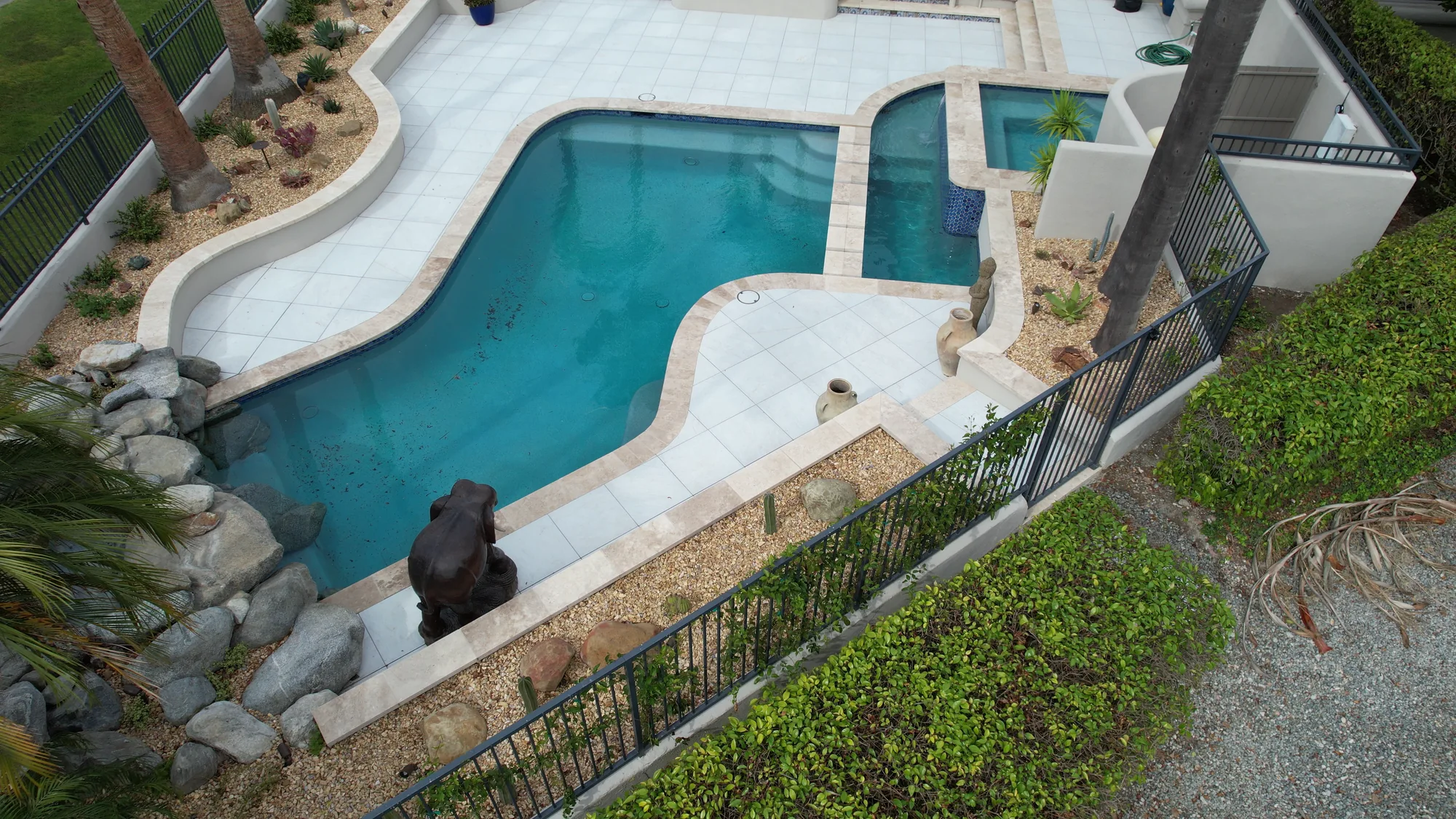 Aerial view of pale paving surrounding a curved pool and raised spa beside the house.