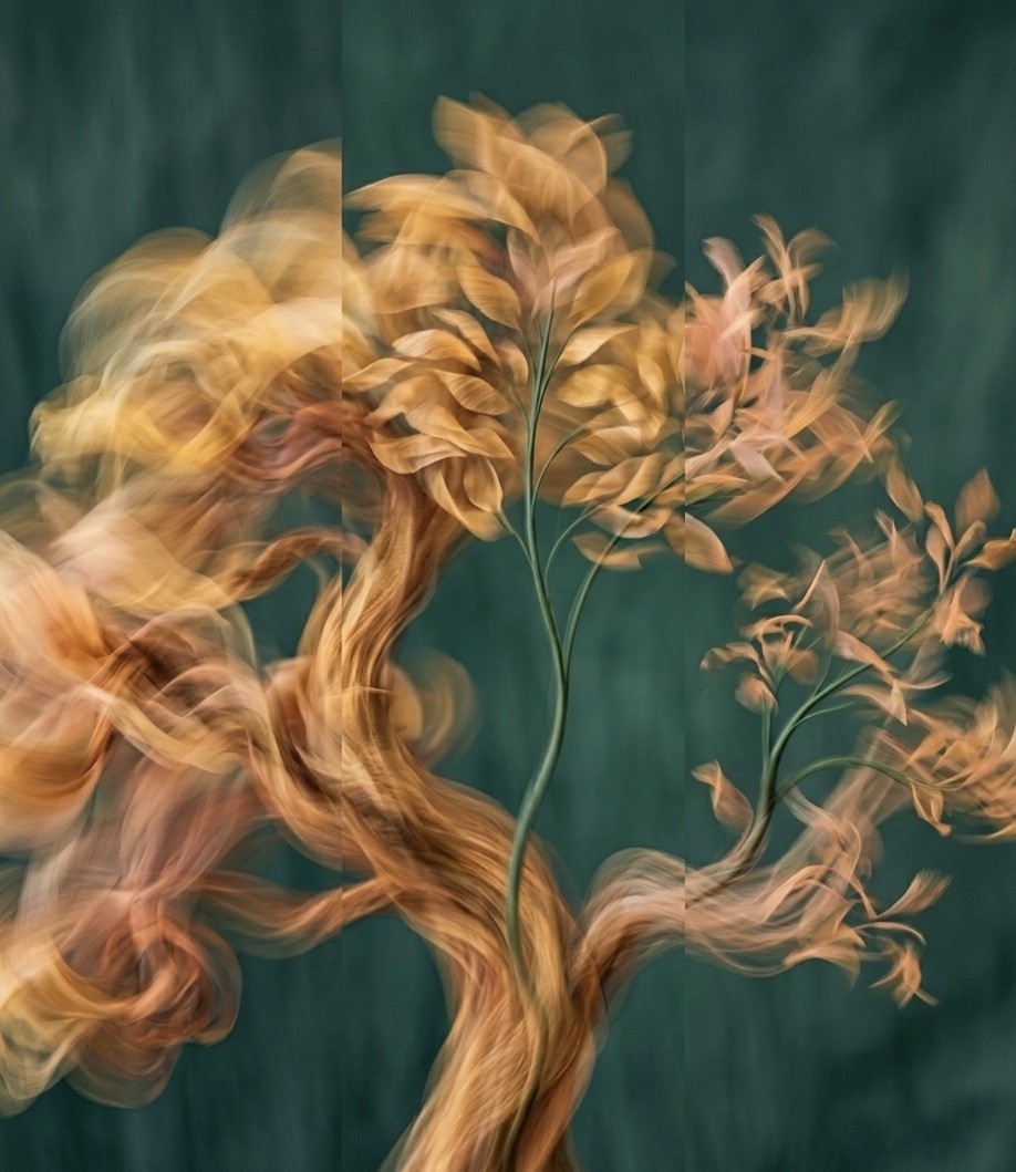Smiling young woman with long hair standing against a dark green background, holding a finger to her chin.
