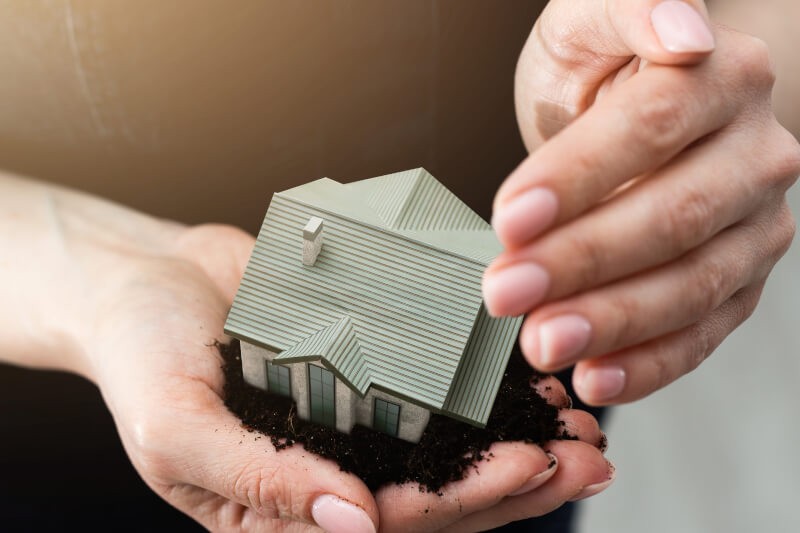 Mână ținând o machetă de casă – protecție completă prin asigurarea locuinței BIXMA.