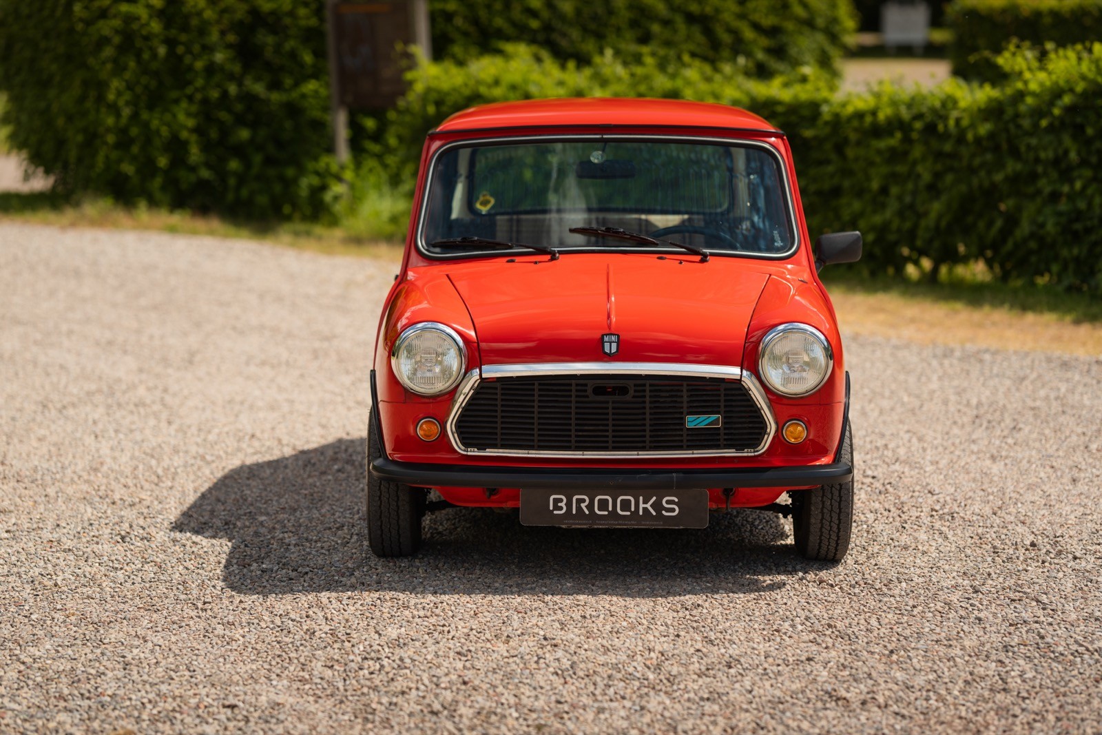A bright red car parked on a gravel driveway, surrounded by greenery and sunlight.
