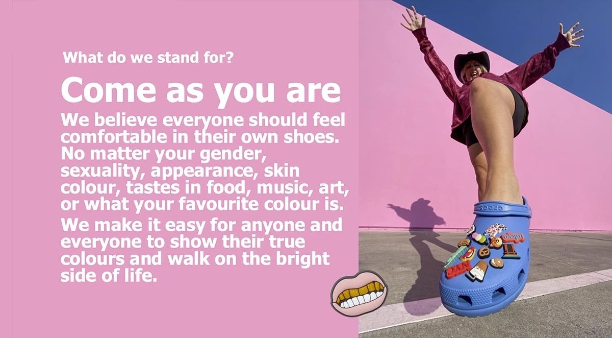 Crocs 'Come As You Are' brand manifesto page showing joyful woman jumping with arms raised wearing blue Classic Clog decorated with Jibbitz charms against pink and blue geometric background, inclusive brand values statement