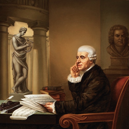 Ein älterer Mann mit weißem Haar sitzt an einem Schreibtisch mit Notenblättern und sieht nachdenklich aus. Eine Statue steht hinter ihm, und Bücher sind in der Nähe gestapelt.