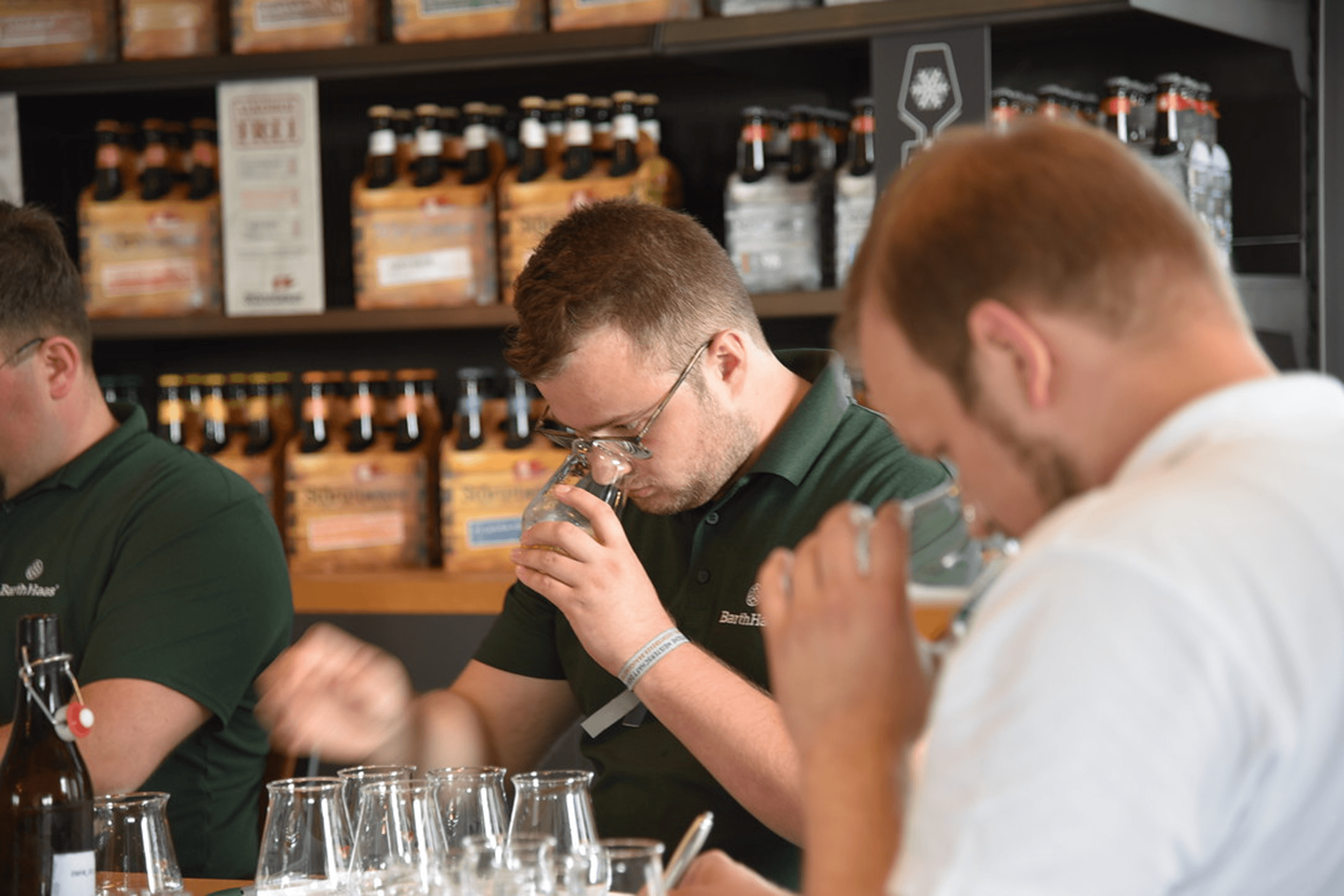 Men taste beverages in front of shelves of beer bottles