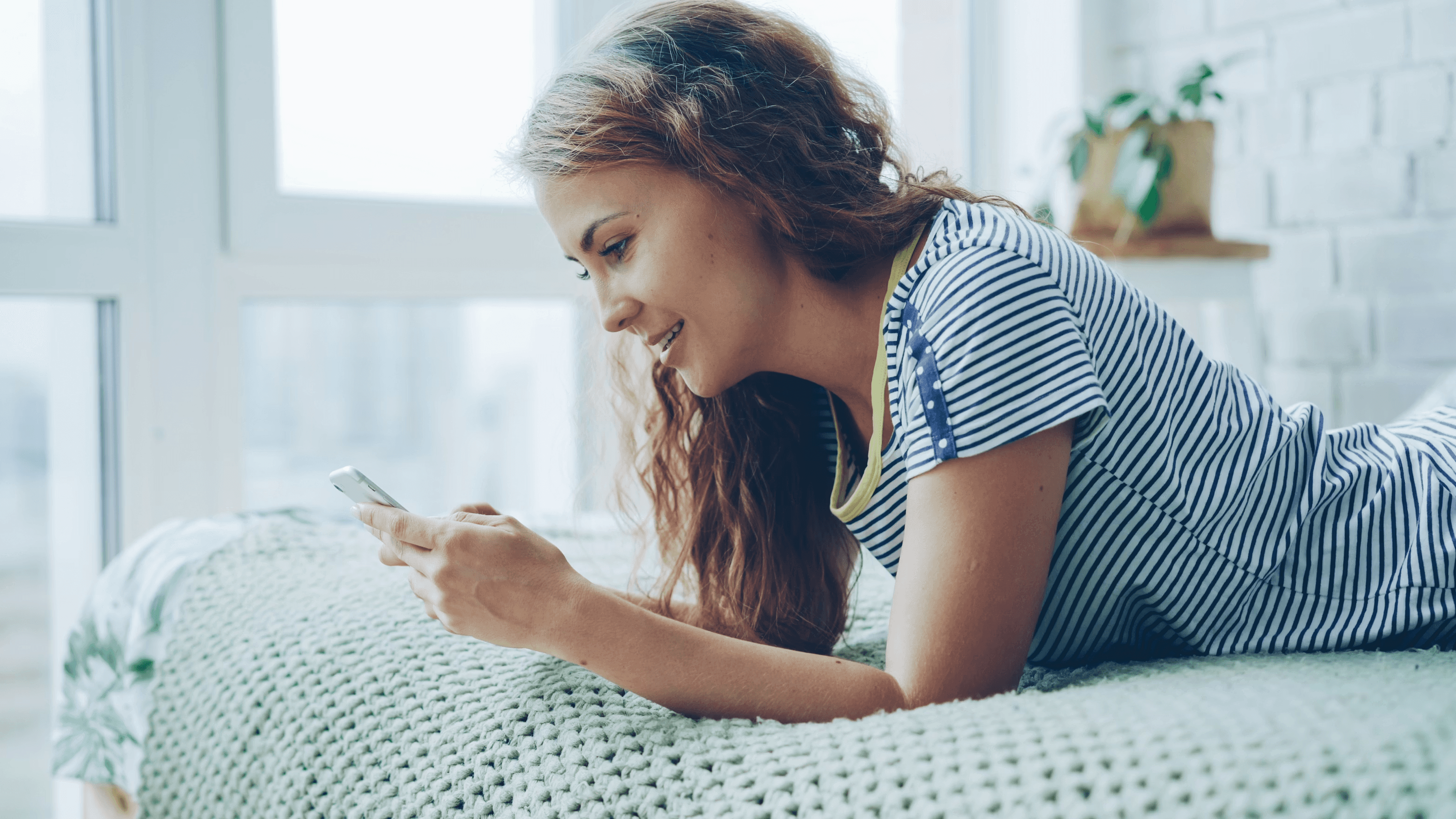 Woman on bed using phone. Smiling and looking at the screen. Modern lifestyle.