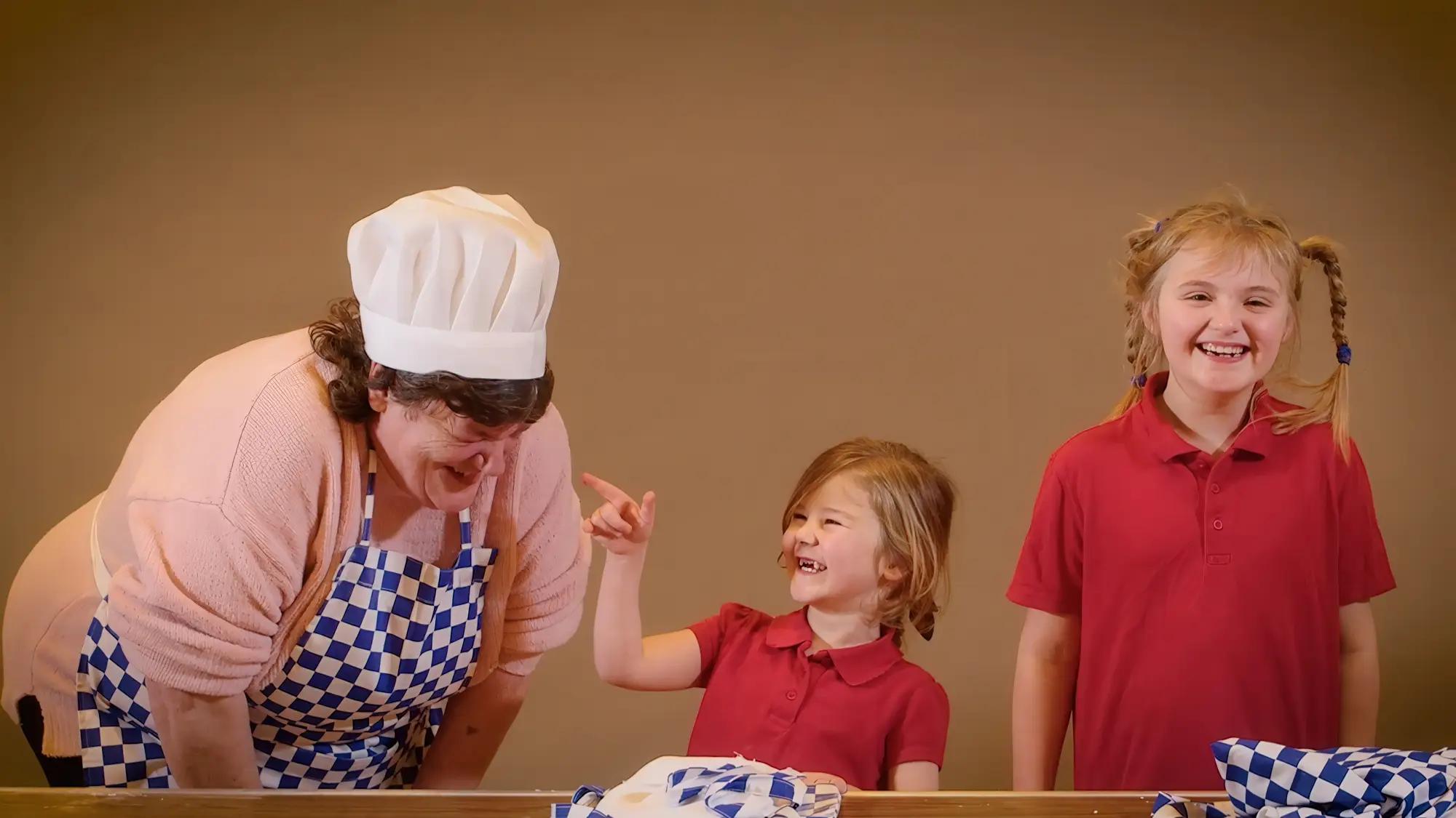 Adult and two children sharing a joyful moment while baking together in a community setting.