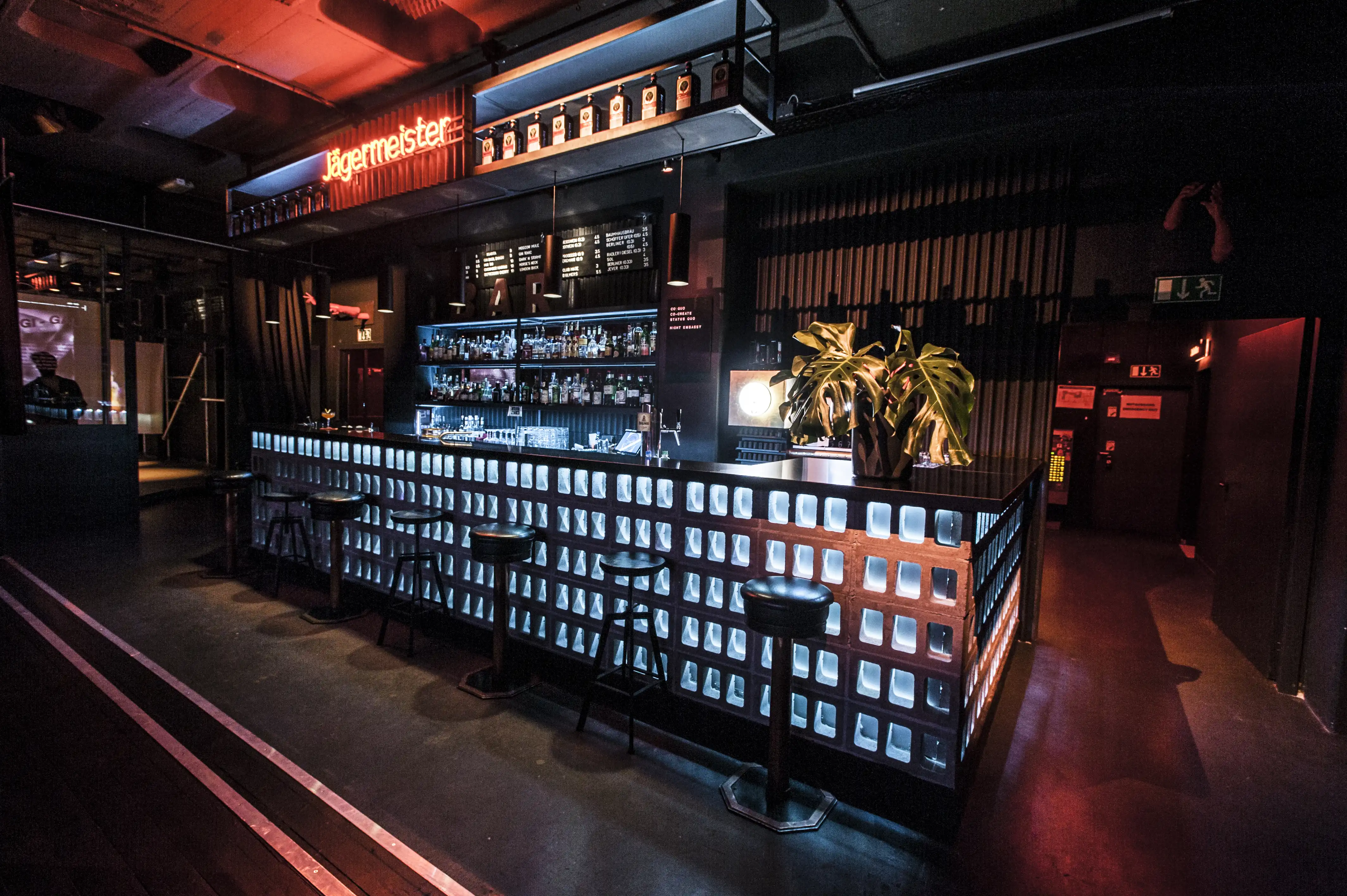 Bar counter built from illuminated Jägermeister bottle crates beneath an orange neon logo at the Night Embassy club.