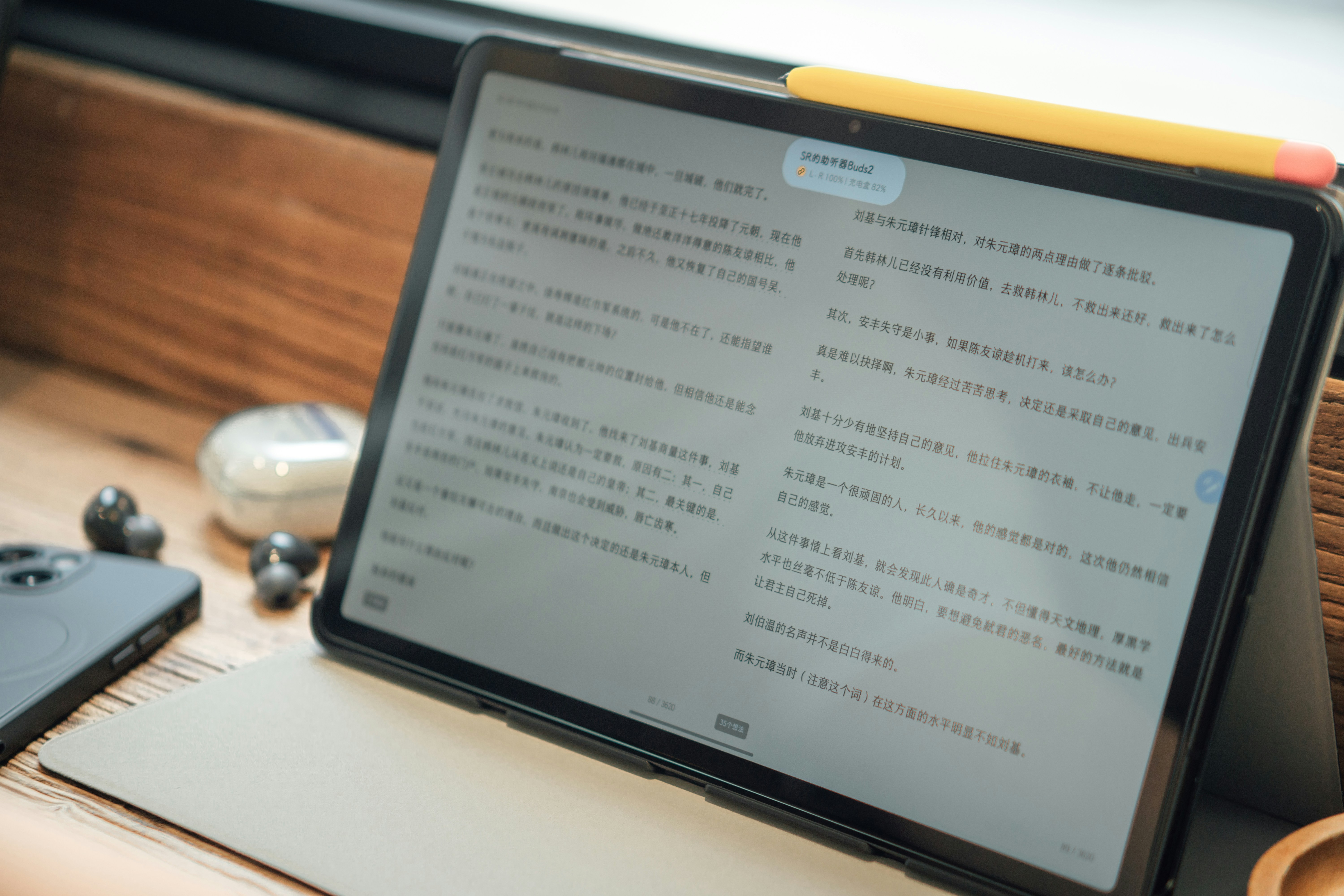 Tablet displaying a document on a desk beside wireless earbuds and a smartphone.