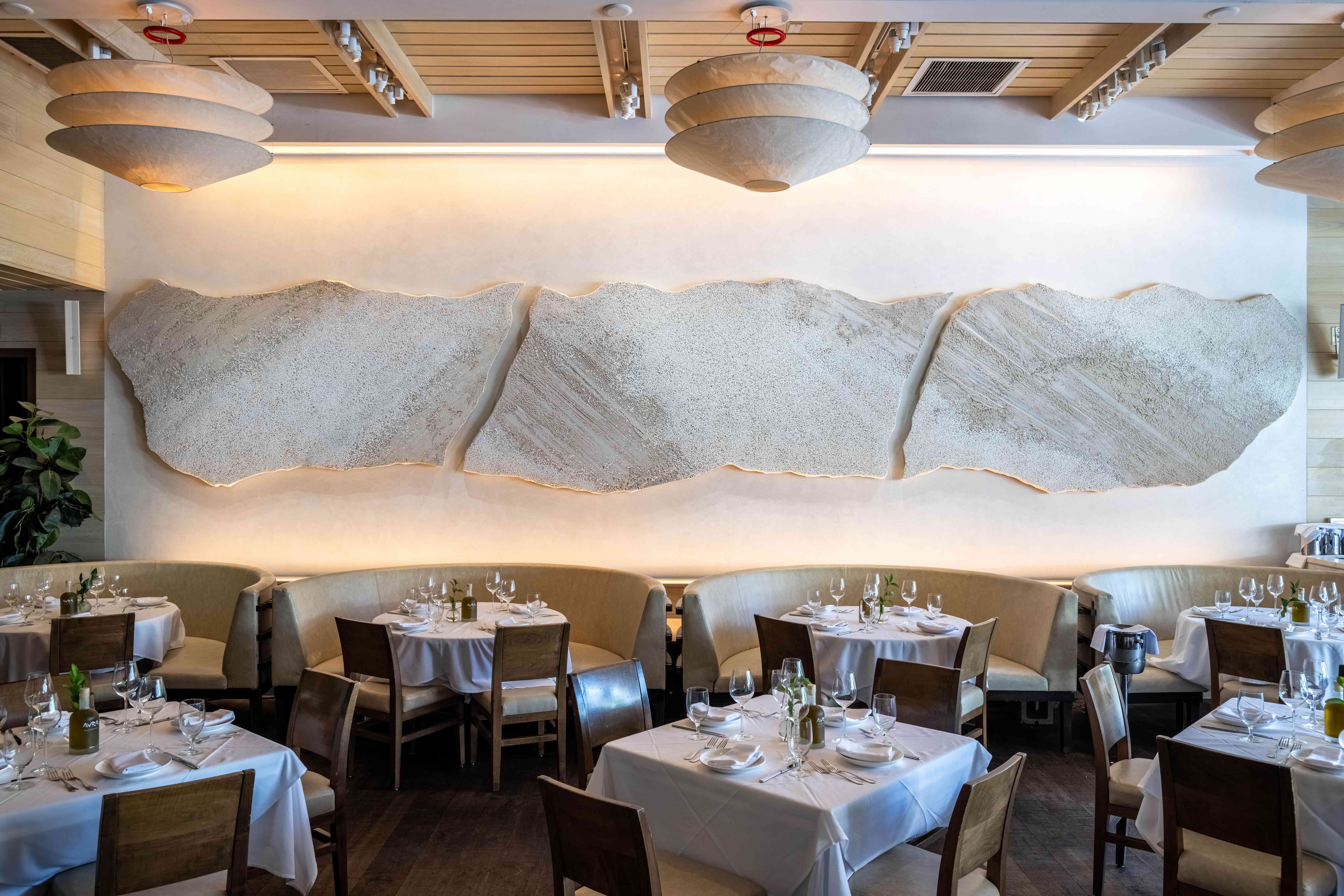 A modern restaurant interior with elegant tables and a large abstract mural on the wall.