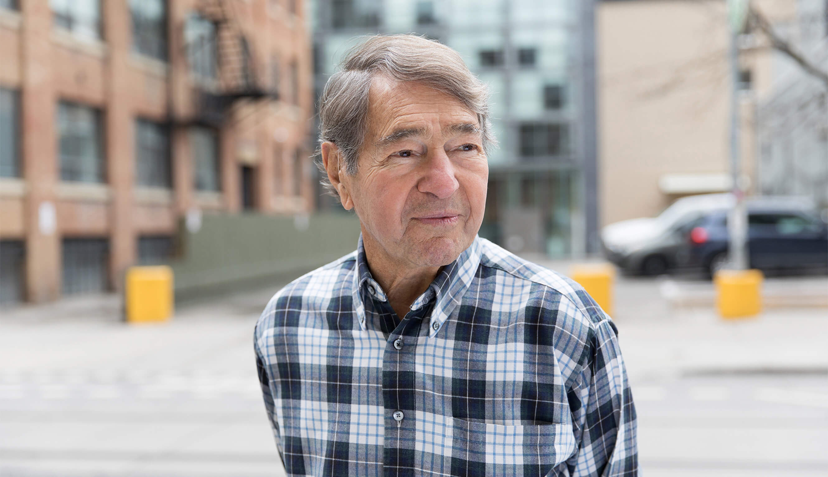 Brightly-lit portrait of the late A.J. Diamond, co-founder of DSA, standing in front of a street in Toronto.