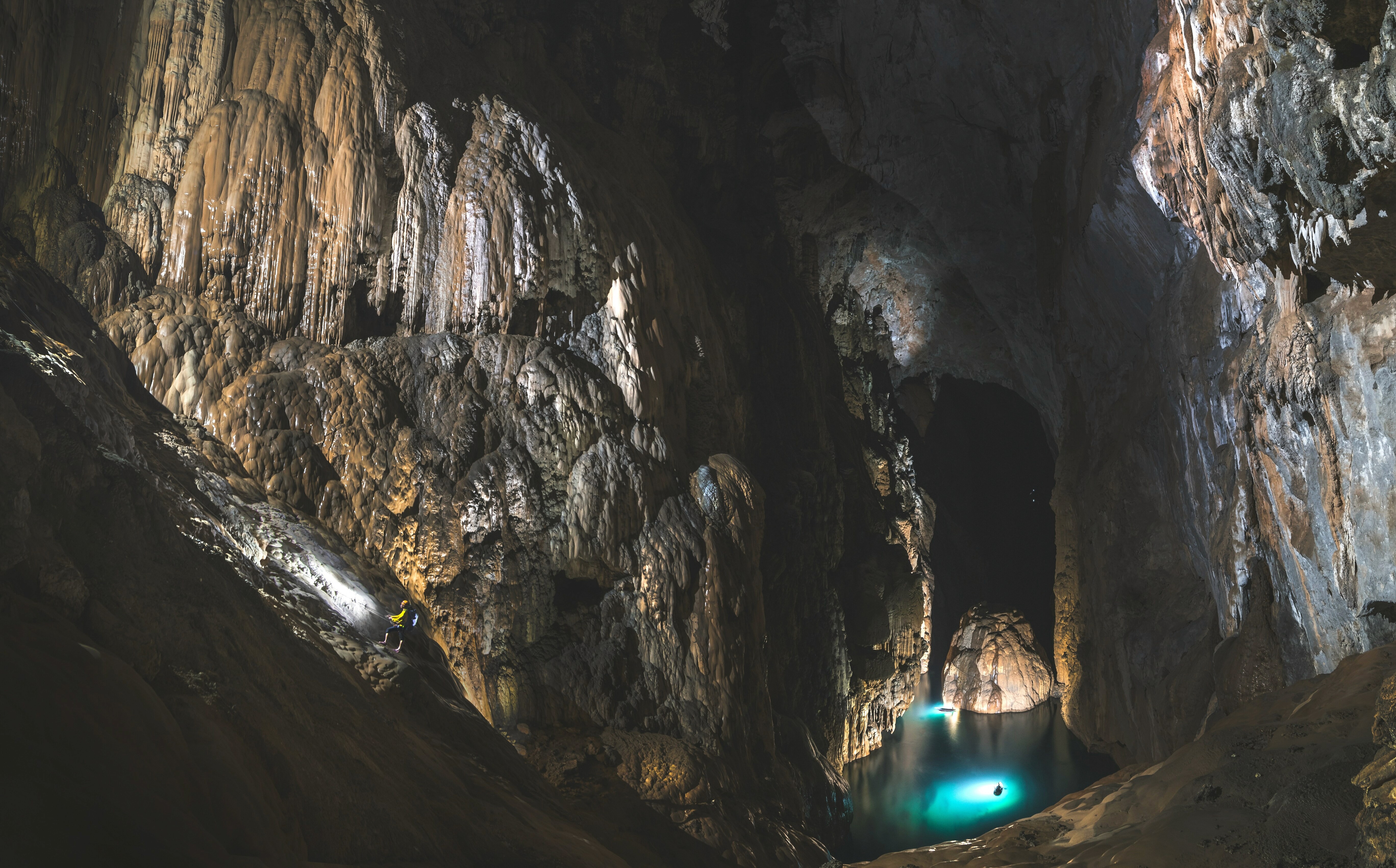 A vast interior view of Son Doong Cave in Vietnam, showcasing colossal limestone formations and a glowing turquoise underground river.