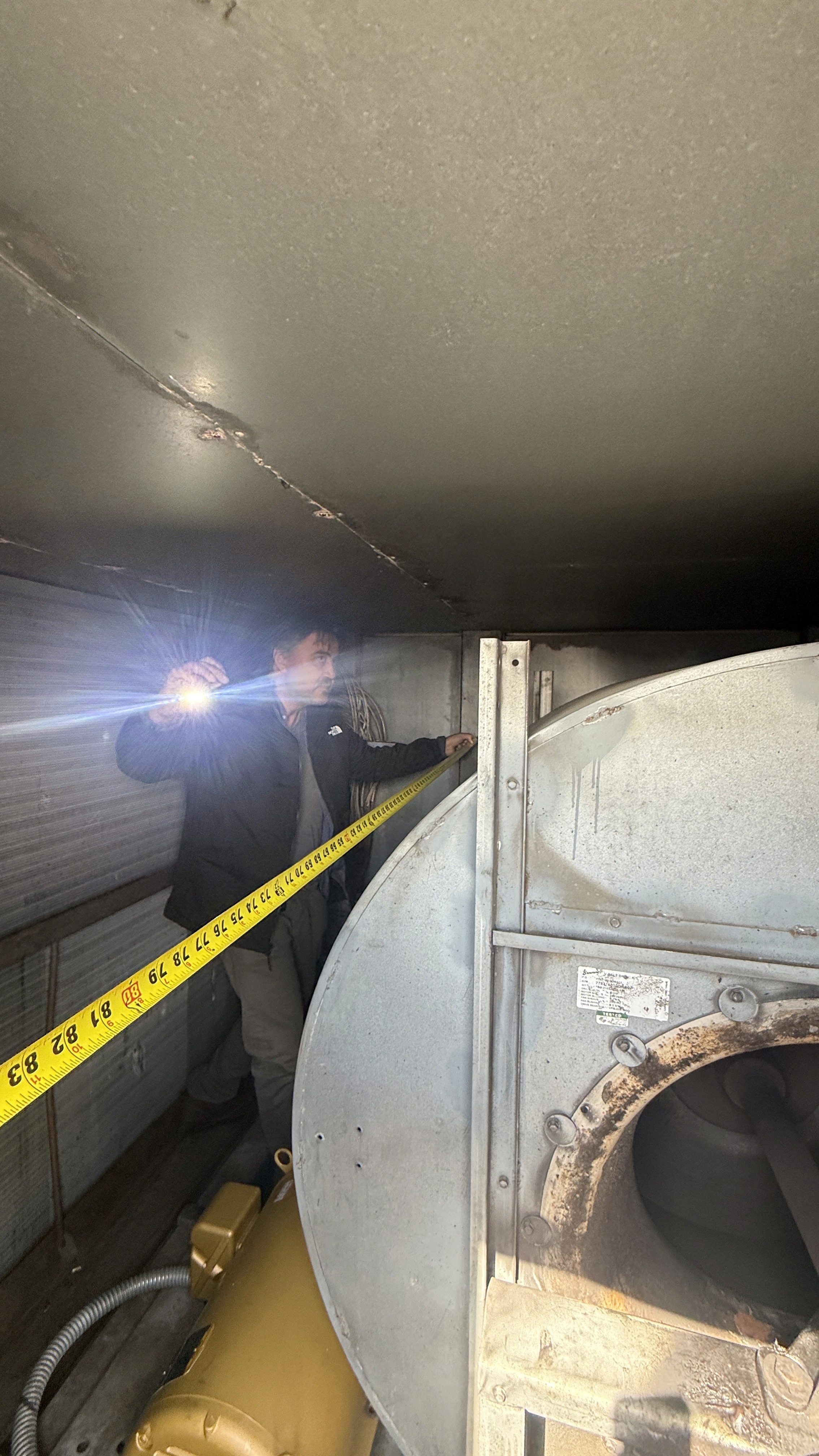 GRR Cooling Experts technician measuring tight access clearance around an existing supply fan during an emergency HVAC retrofit in a critical NYC healthcare environment