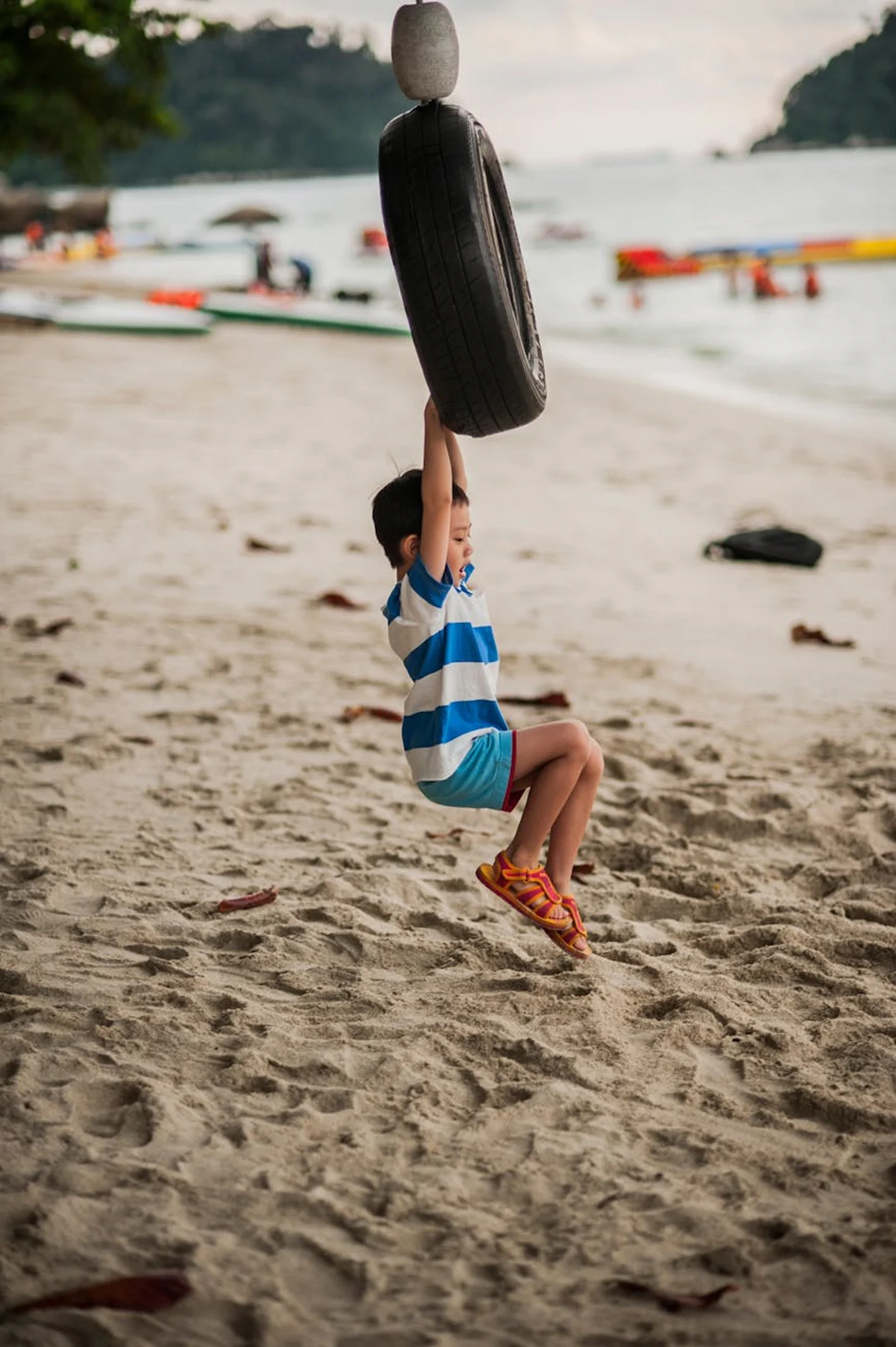 A child carrying a bodyboard while walking on a sandy beach.