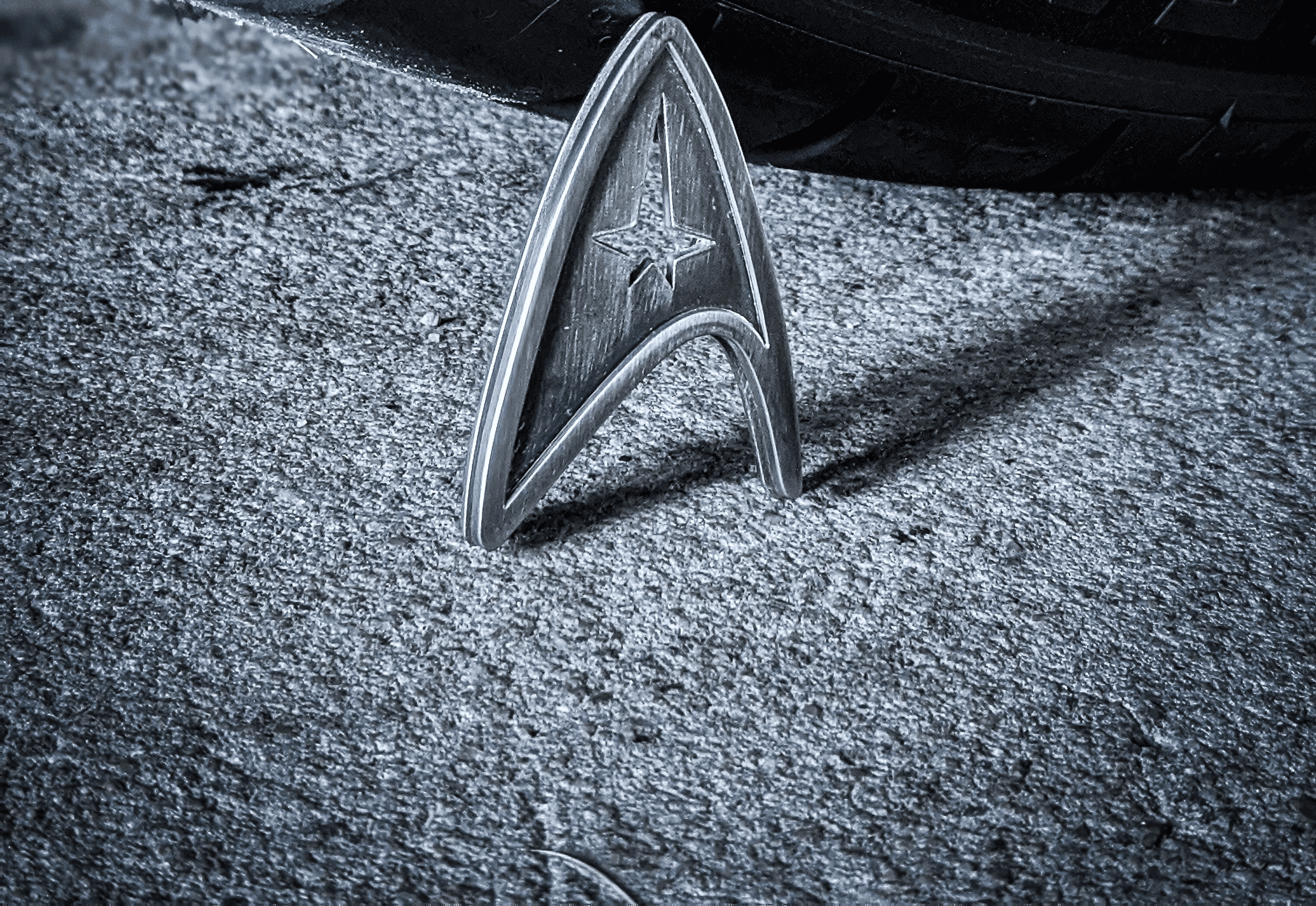 A silver Star Trek insignia badge against a grey background