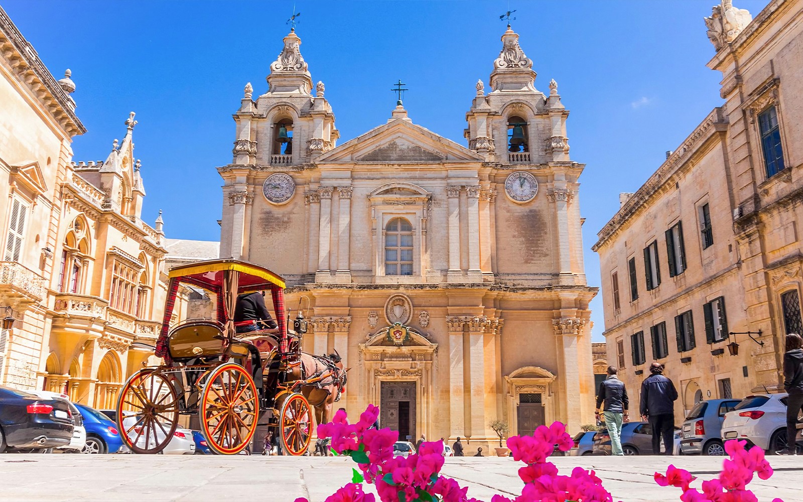 Historic building in Mdina with horse-drawn carriage and pink flowers in foreground.