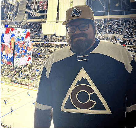 Brian at a Colorado Avalanche Game wearing a jersey and ball cap