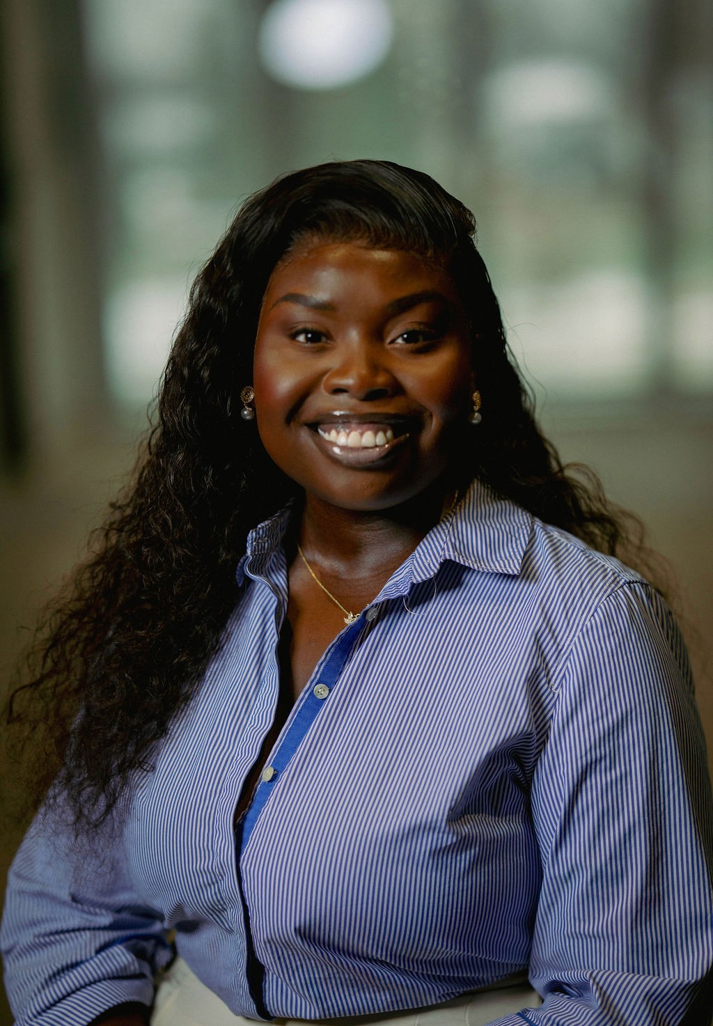 Portrait of a person with red hair, wearing a rust-colored outfit and scarf, set against a neutral gray background.