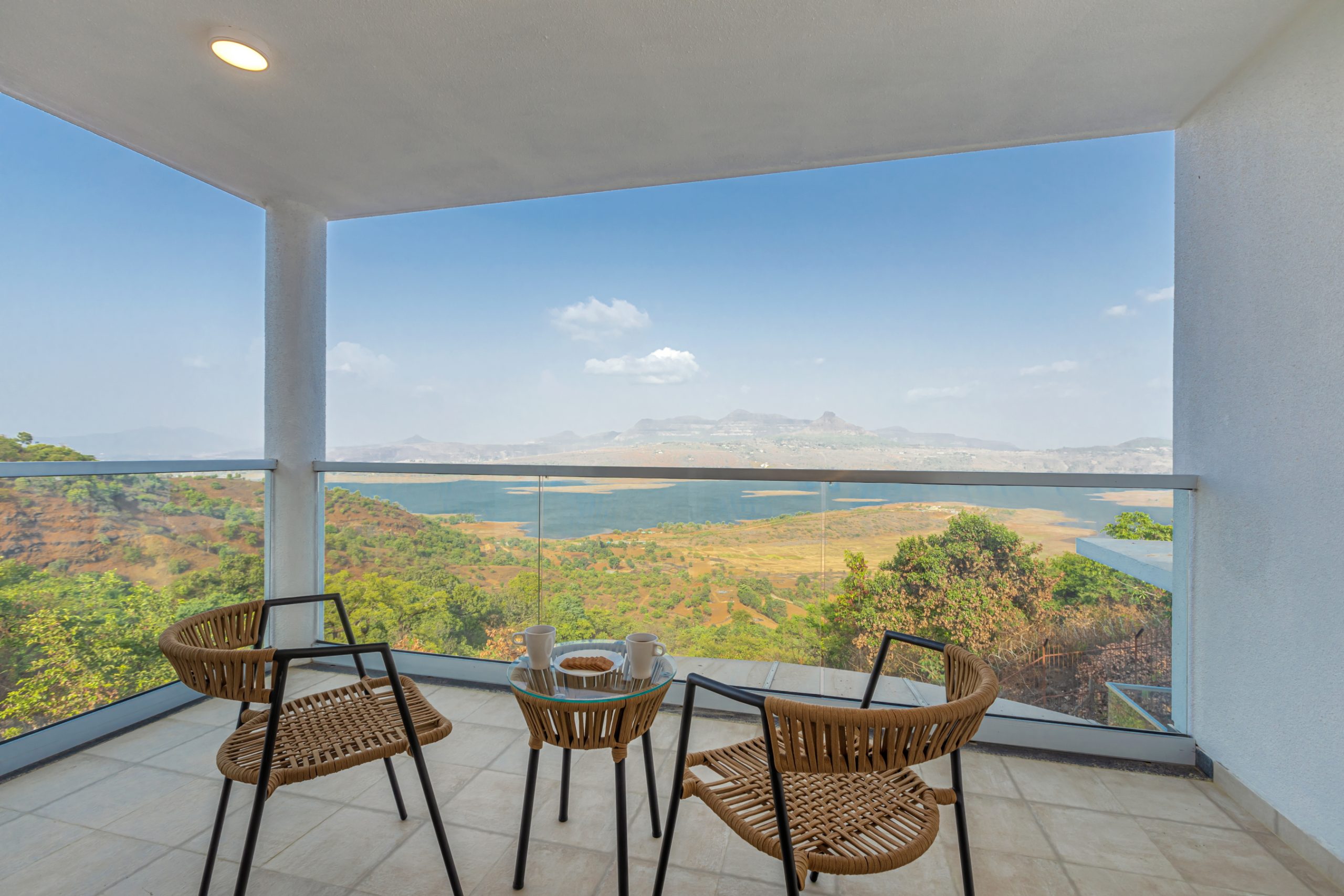 <img src="your-image.jpg" alt="Two wicker chairs and a small table with cups sit on a tiled balcony, overlooking lush greenery, distant mountains, and a clear blue sky—perfect for a serene second home retreat.">