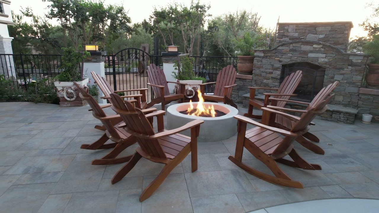 A circular fire feature with wooden chairs on a paved patio, with curved steps and planting around the seating area.