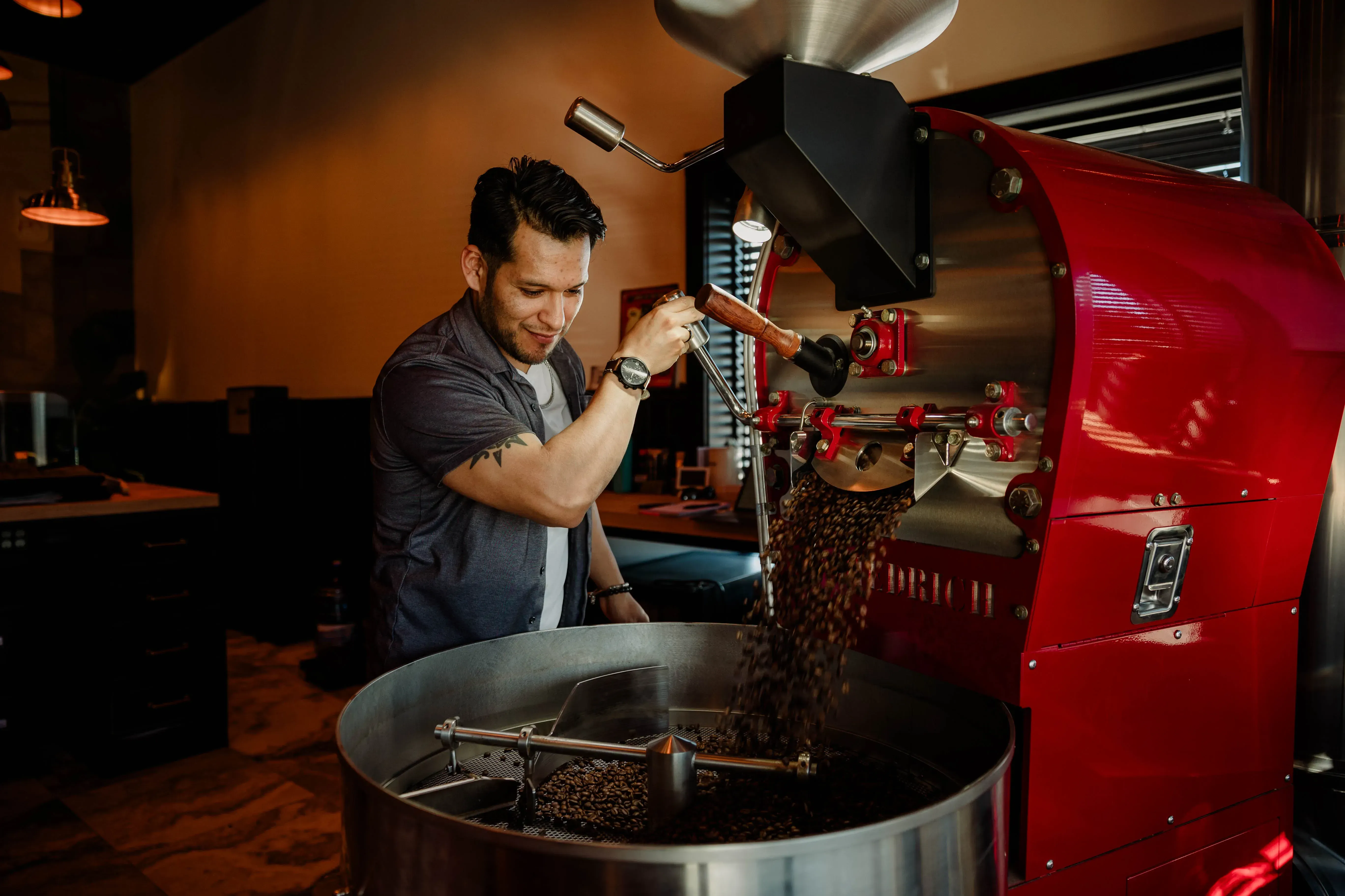 Pain d'Avignon roaster operating the red coffee roasting machine — freshly roasted beans cascading into the cooling tray