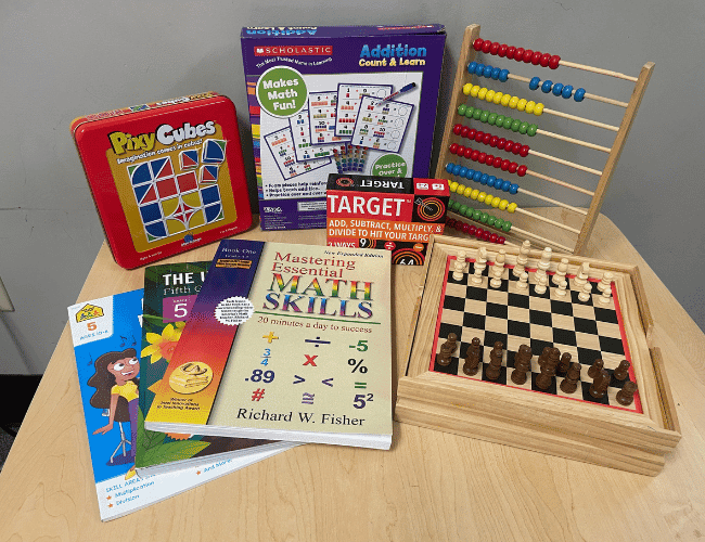 Some math workbooks, math and memory games, chessboard with chess pieces, and abacus on a table in our learning room at SportPlus Charlotte