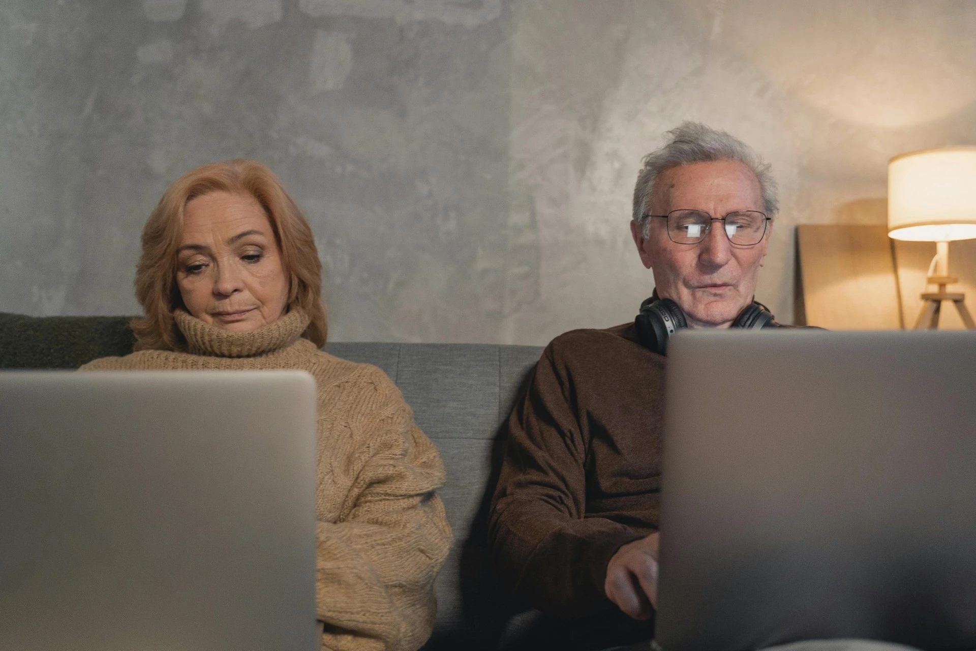 An older couple sitting together on a couch at home, each focused on their own laptop screen, representing employees researching individual retirement savings options and PEO employer-sponsored plans.