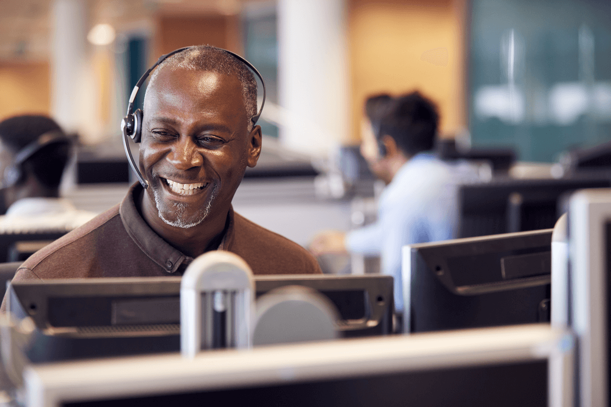 customer onboarding: Smiling man wearing a headset while looking at his monitor