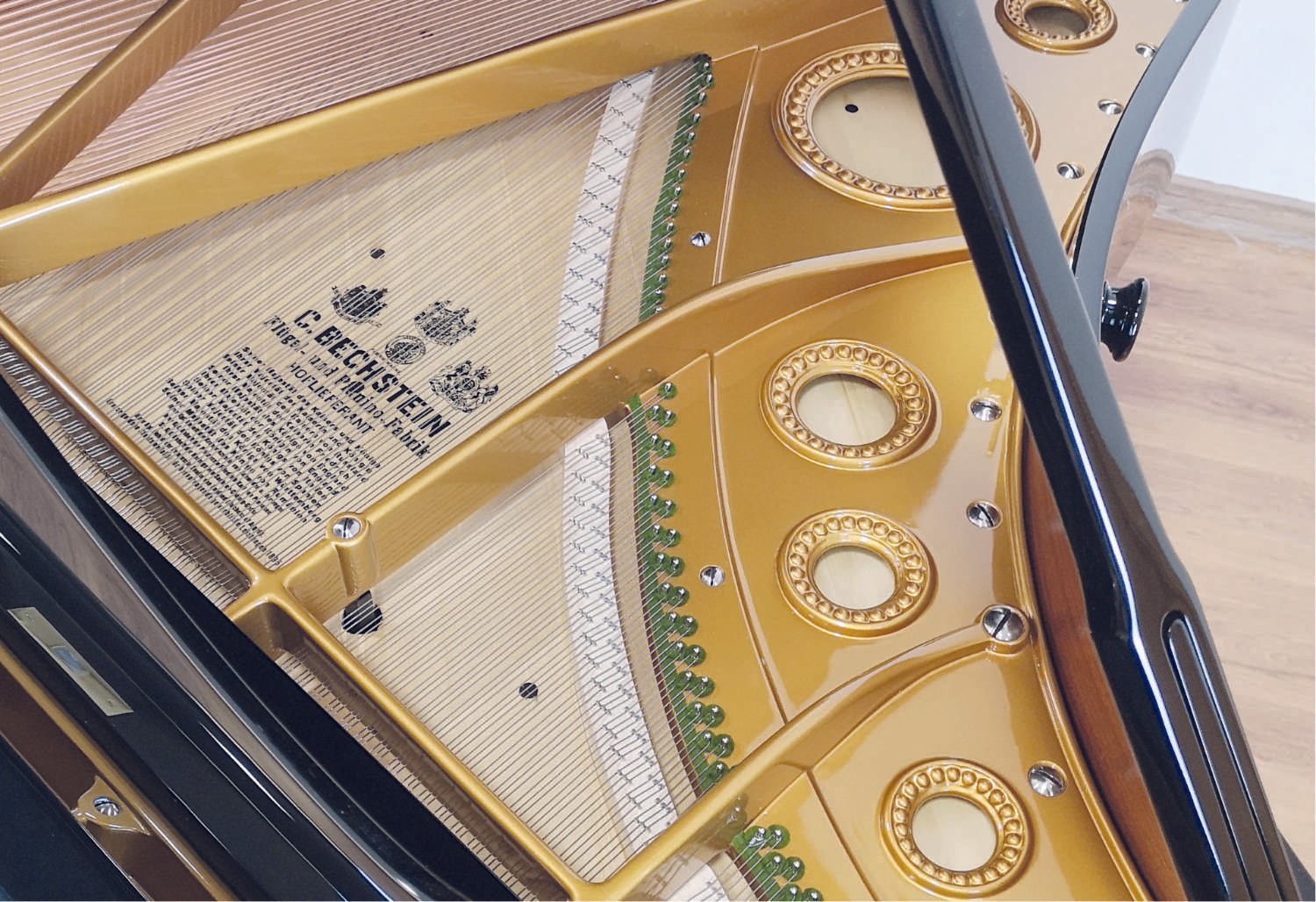 A close-up of the golden interior frame of a restored C. Bechstein piano, showcasing fine details of the string arrangement.