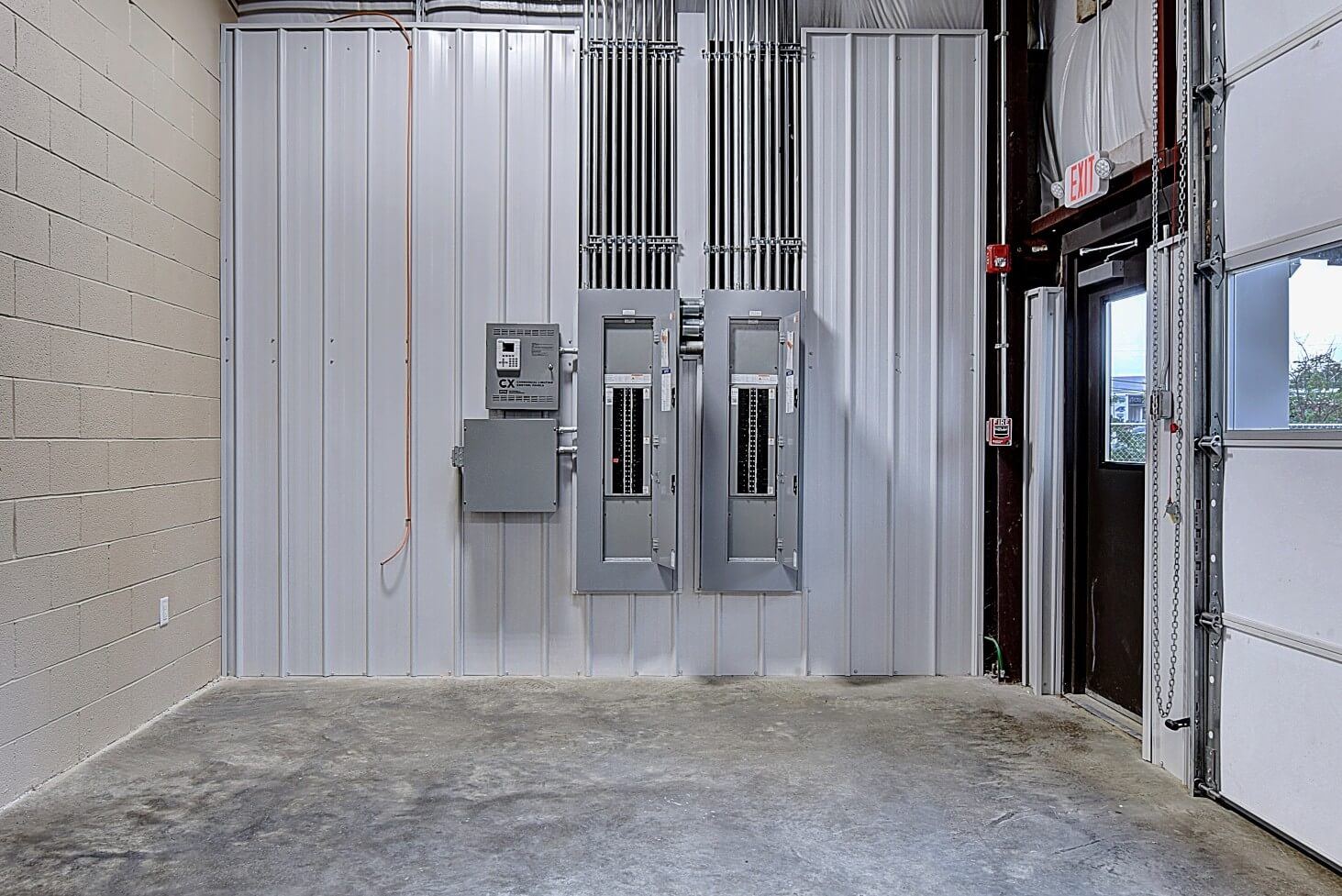 Empty industrial space with white walls, concrete floor, and electrical panels on one side.