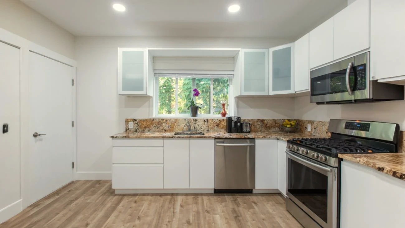 Modern custom kitchen in Vancouver multiplex featuring white flat-panel cabinets, granite countertops, stainless steel appliances, and engineered hardwood flooring with natural light