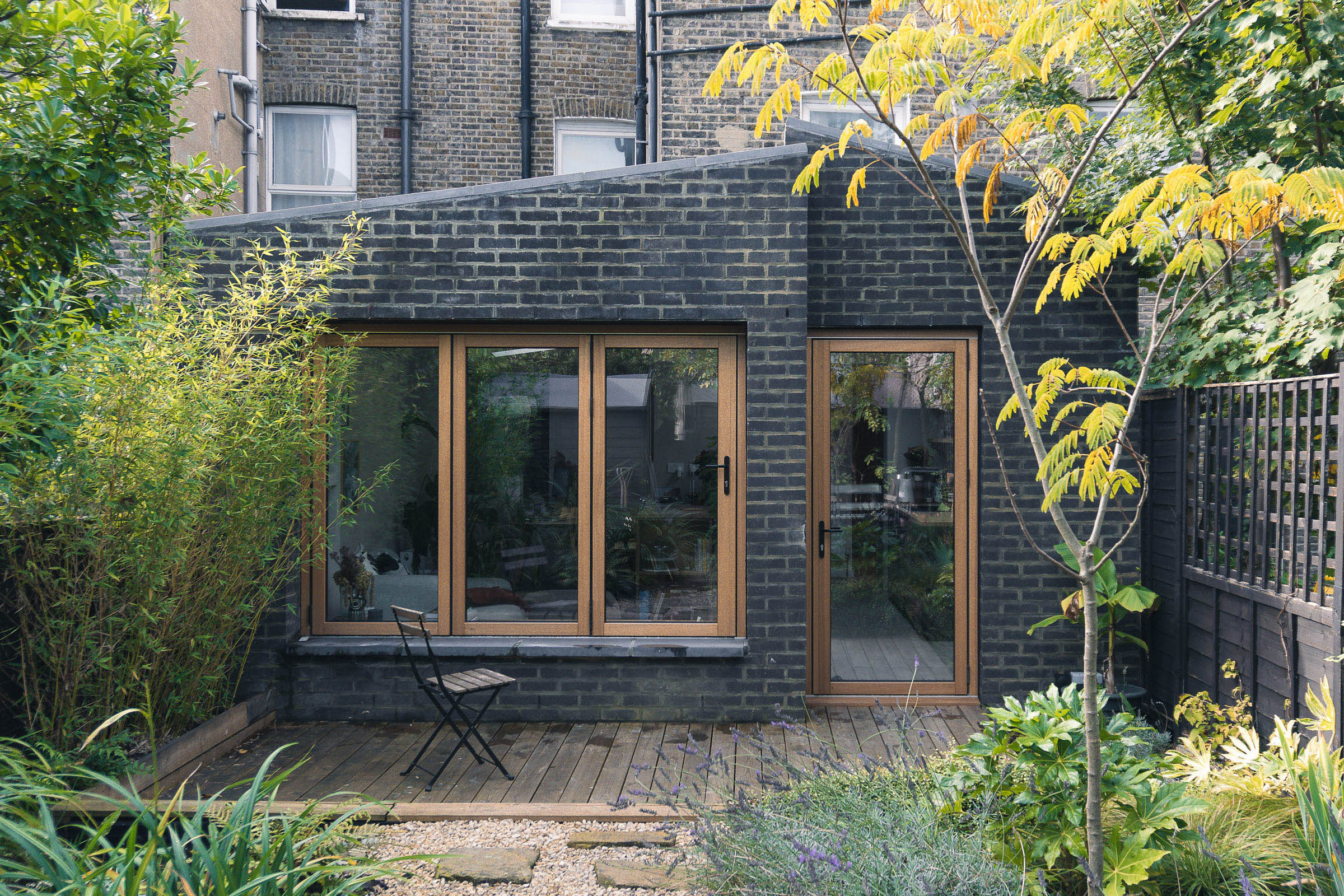 Rear garden view of dark brick extension with timber bifold doors and deck, Shardeloes Road Brockley — Alec Crisp Architects Bristol