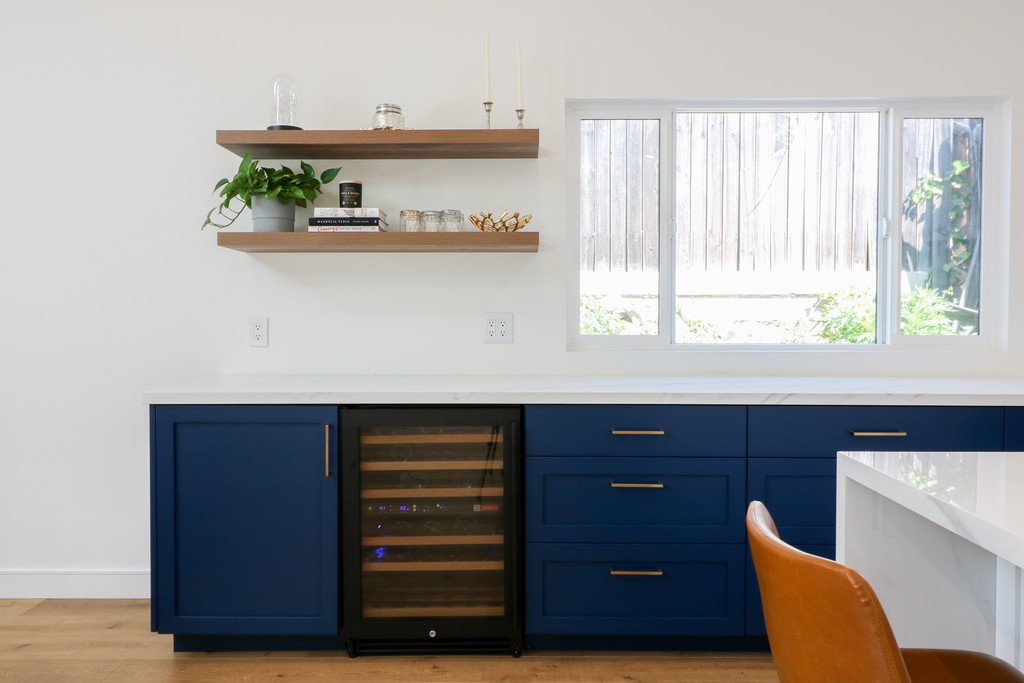 navy blue cabinetry wtith two dark oak floating shelves and wine cooler