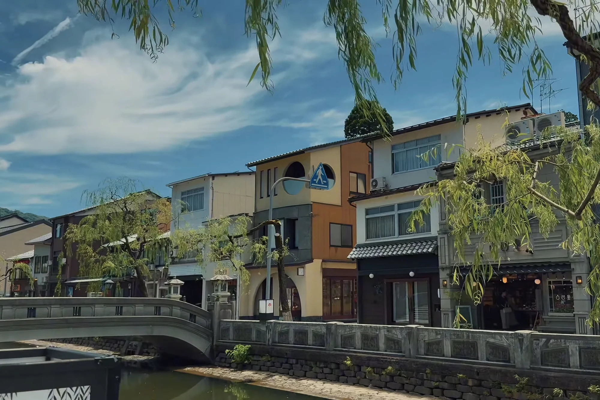 The Kinosaki canal in summer with deep green willows over the water.