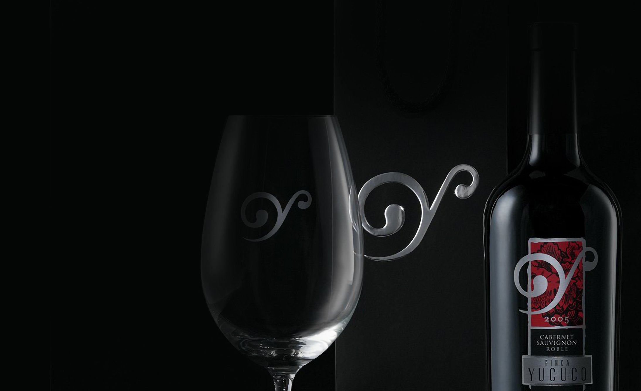 A wine glass with a decorative swirl facing a Cabernet Sauvignon bottle. Both are set against a dark background, conveying elegance and sophistication.
