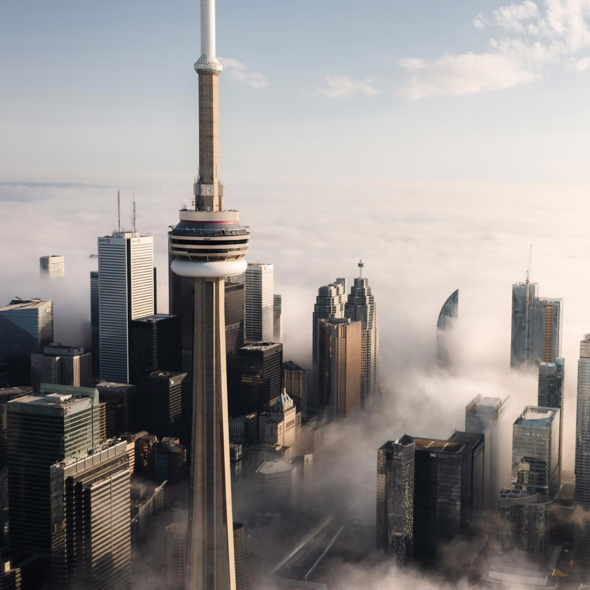 Skyscraper tower rises above urban skyline with clouds and clear sky.
