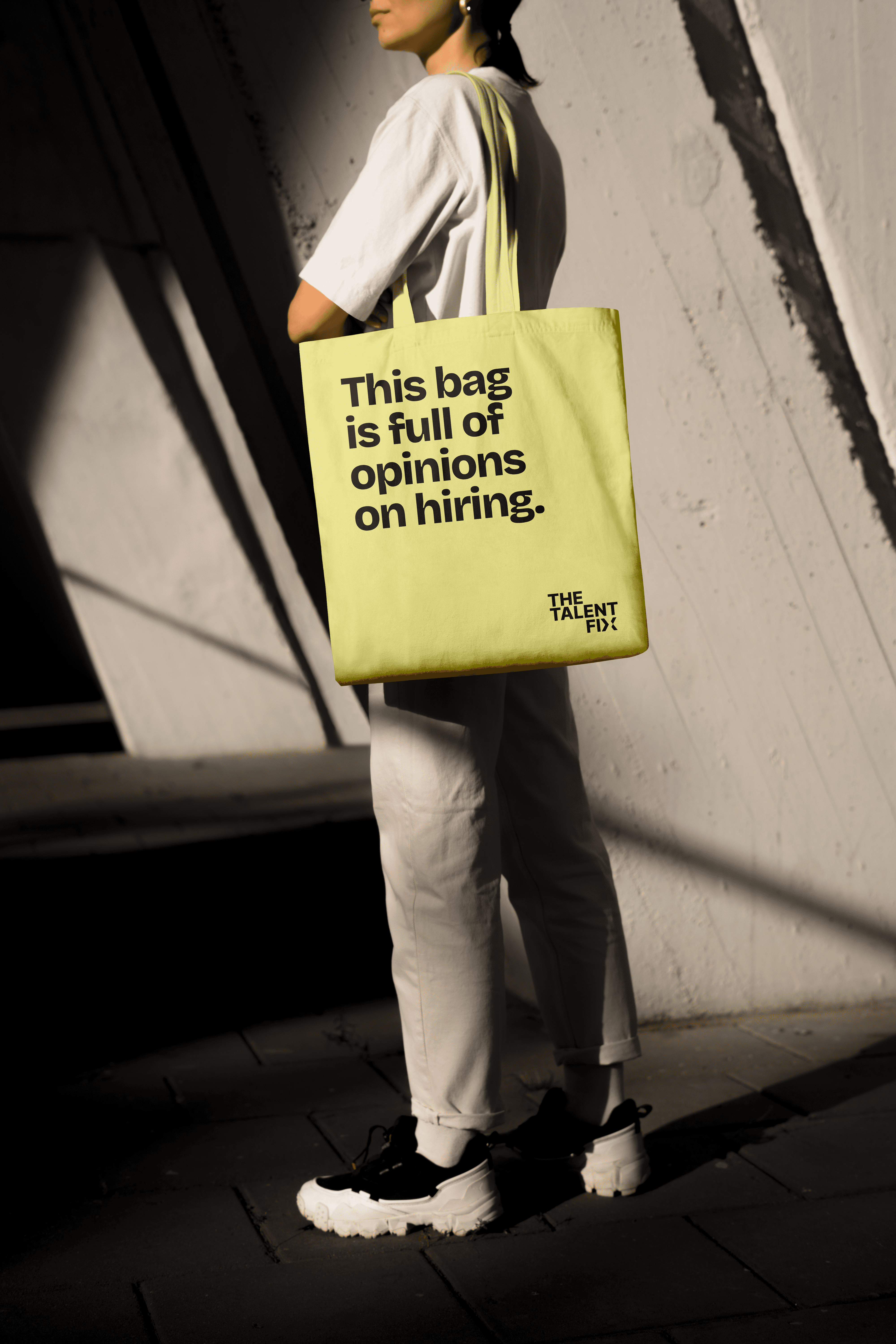 A person stands against a wall, holding a bright yellow tote bag with a motivational phrase printed on it.