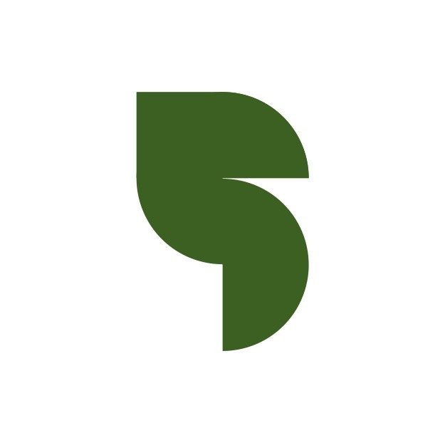 A woman with blonde bob hair in a grey coat and beige turtleneck stands against a neutral backdrop. She has a serious expression, conveying elegance.