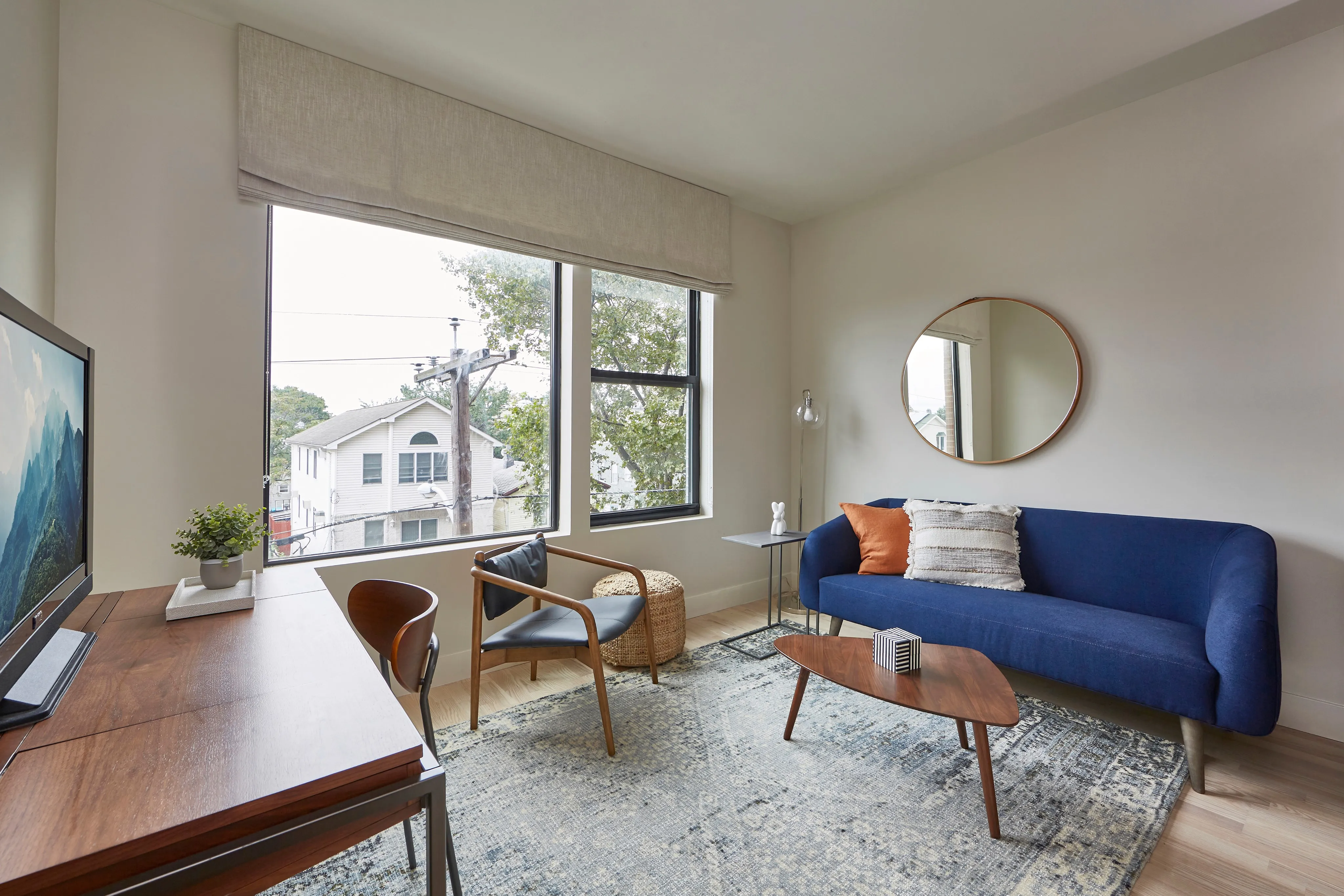 Cozy living room with a blue sofa, wooden table, and large window letting in natural light.