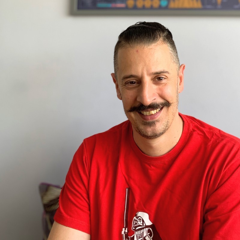 A young person with short, light-colored hair and glasses is looking directly at the camera.