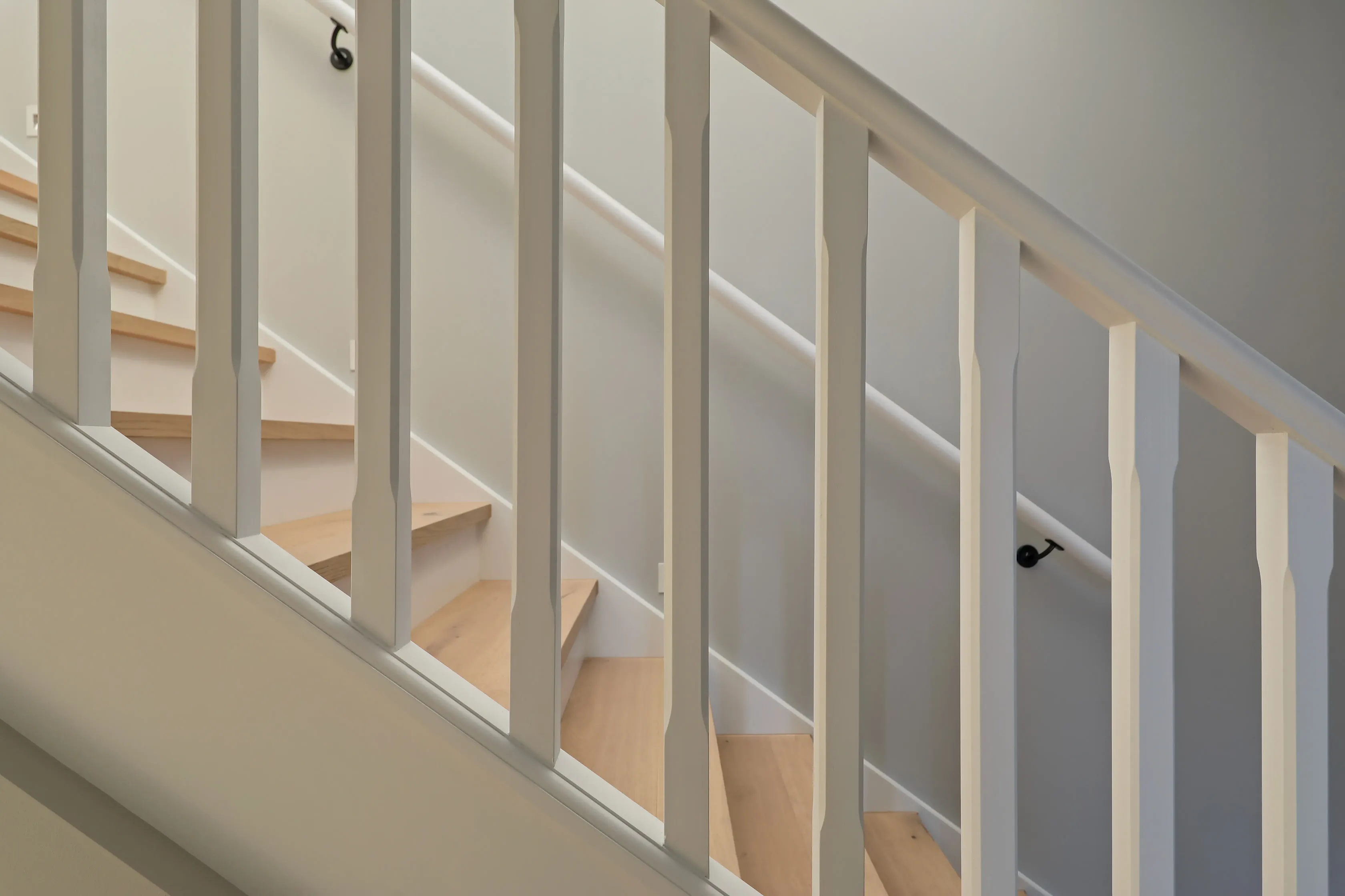 Detail of the staircase with pale grey square balusters, a timber handrail, black wall brackets and light oak treads