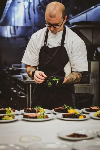 Chef in black apron plating dishes at a stainless steel kitchen station
