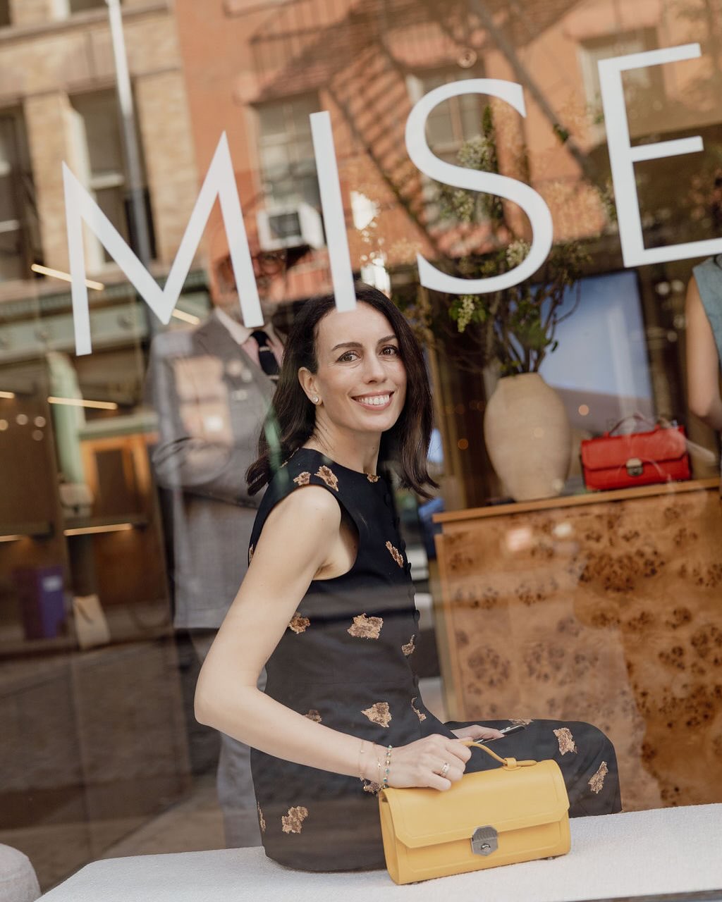 Misela founder seated inside the Bond Street boutique window with vinyl storefront signage and handbag display.