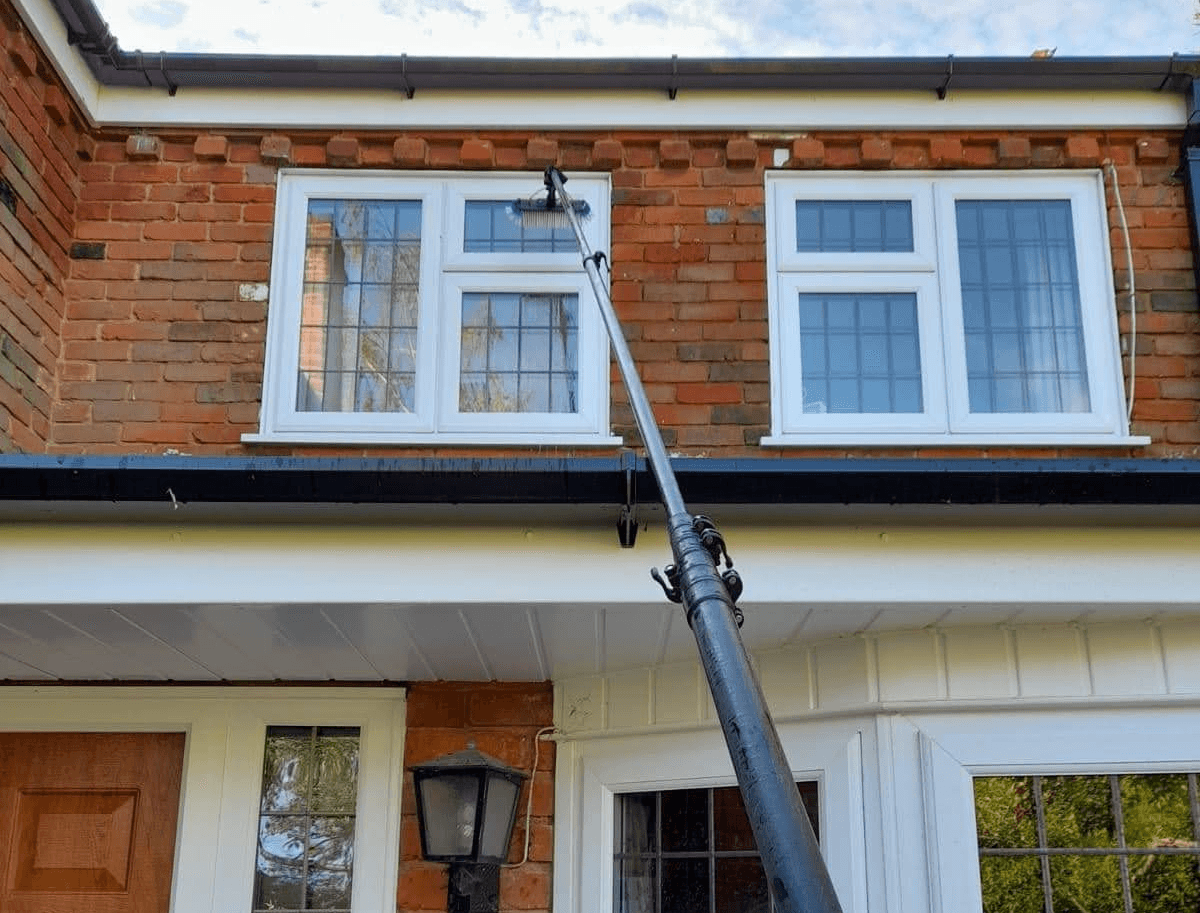 Professional window cleaner using water-fed pole system on a residential home in North London