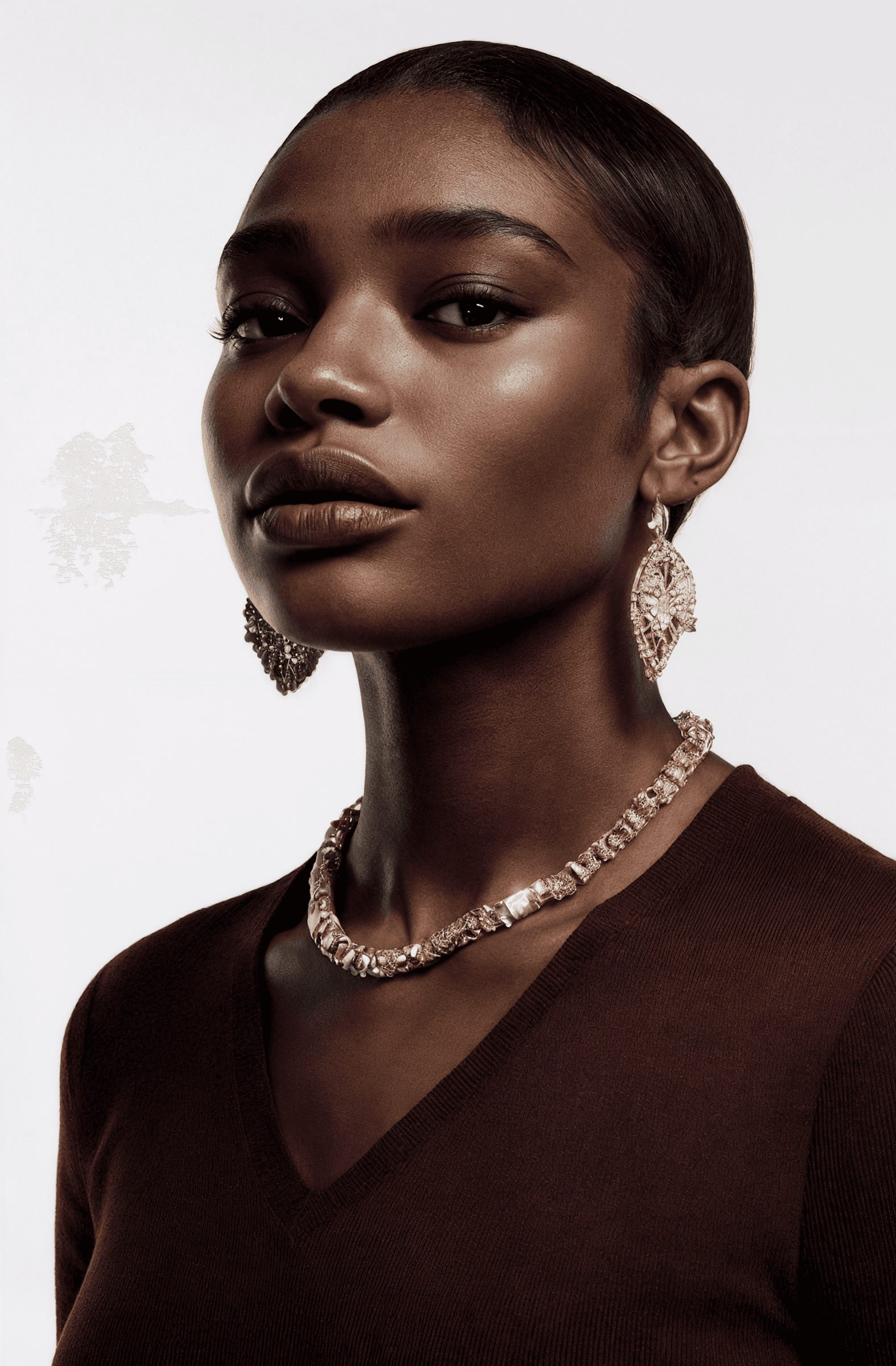 A striking portrait of a woman wearing gold jewelry and a burgundy top, set against a clean white background.