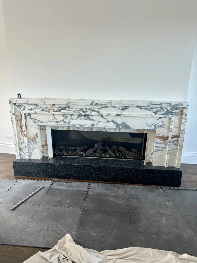 Natural stone fireplace surround with marble mantel, black hearth, and detailed feature wall cladding.