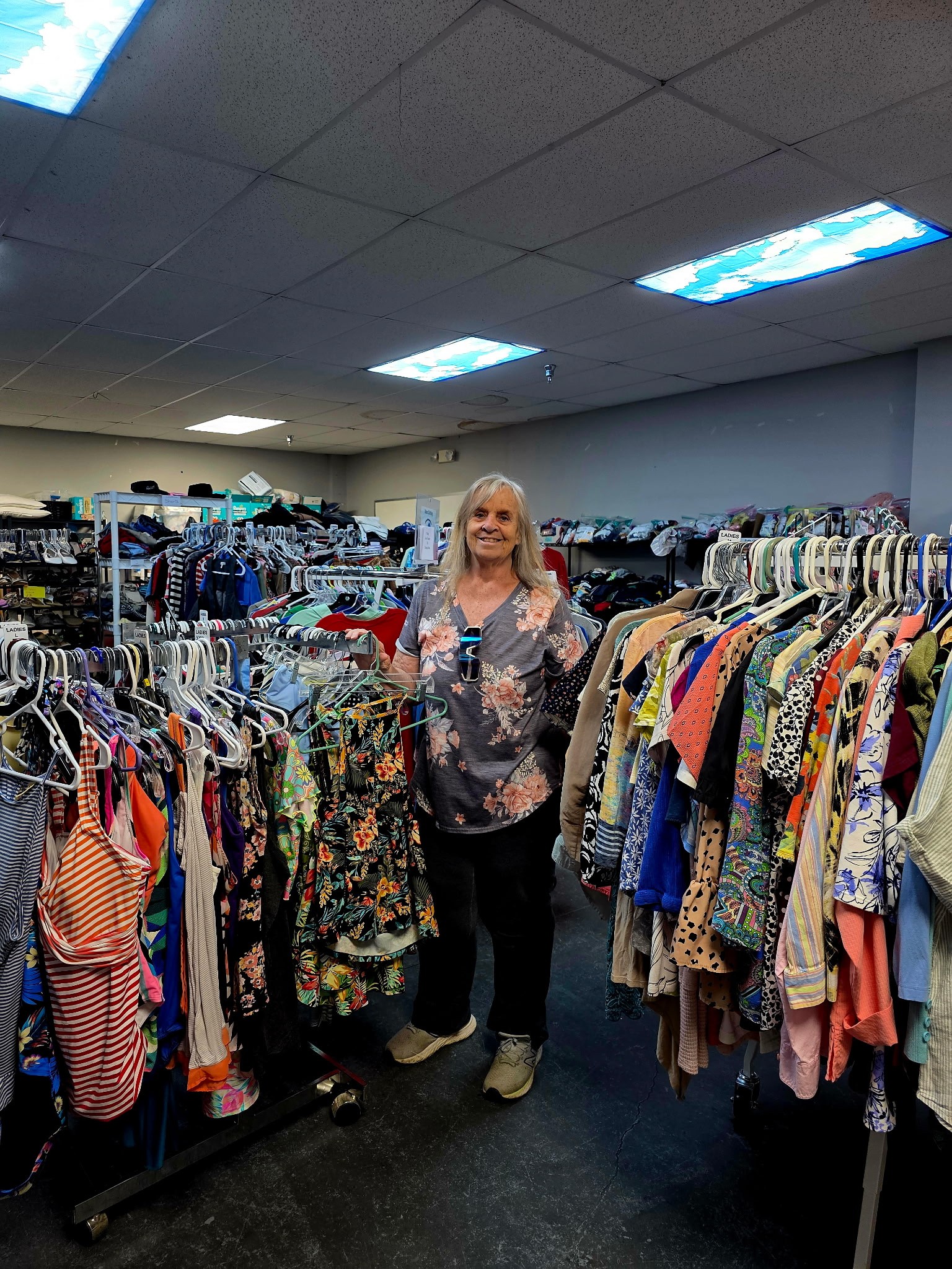 Store manager Susan Morgan stands smiling among racks of donated clothes inside the Clothed in Kindness free clothing store in Jefferson County, Indiana.