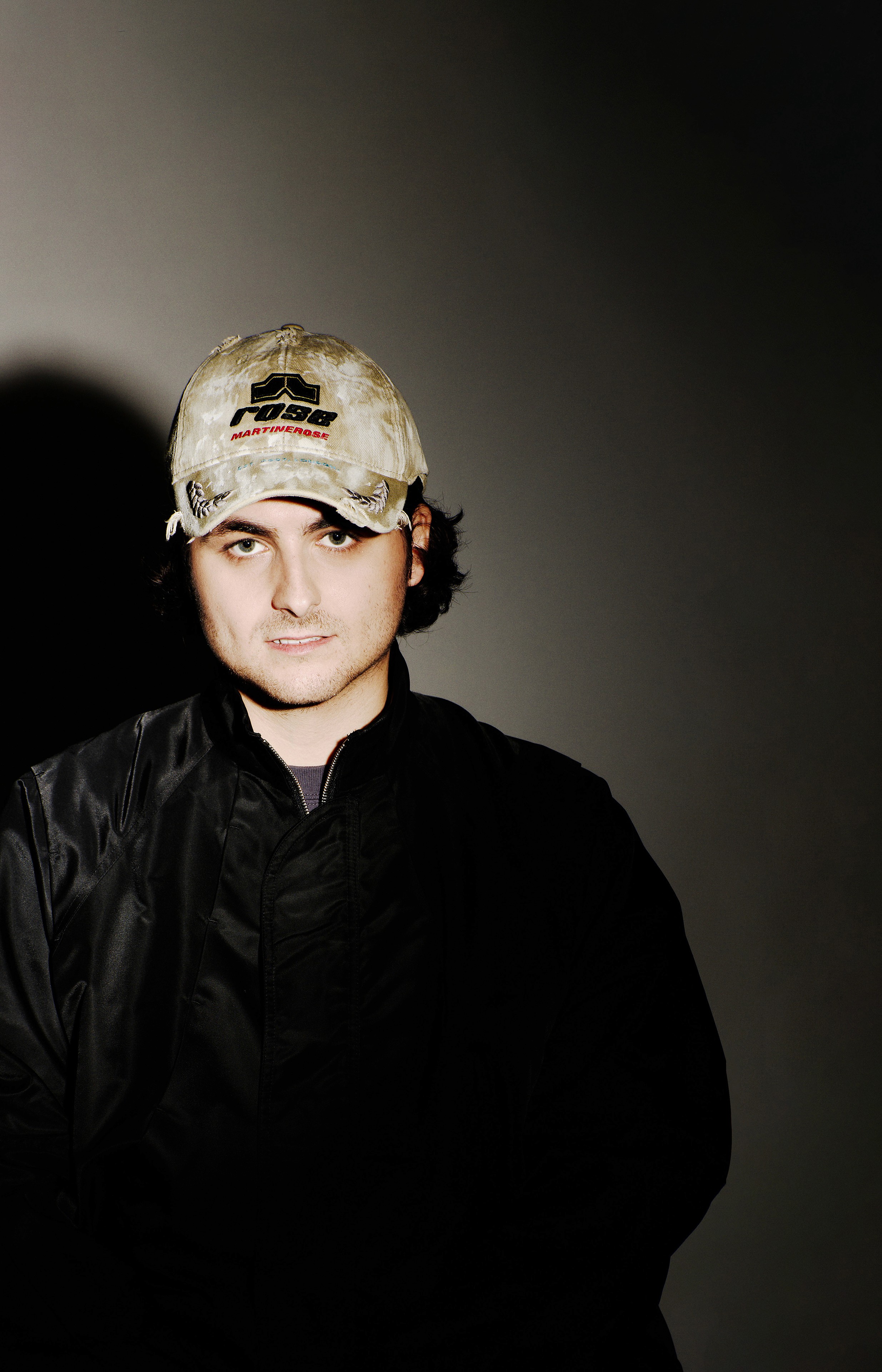 Portrait de l'artiste Notre Dame portant une casquette de baseball et un blouson sombre, avec un éclairage dramatique mettant en avant son regard.